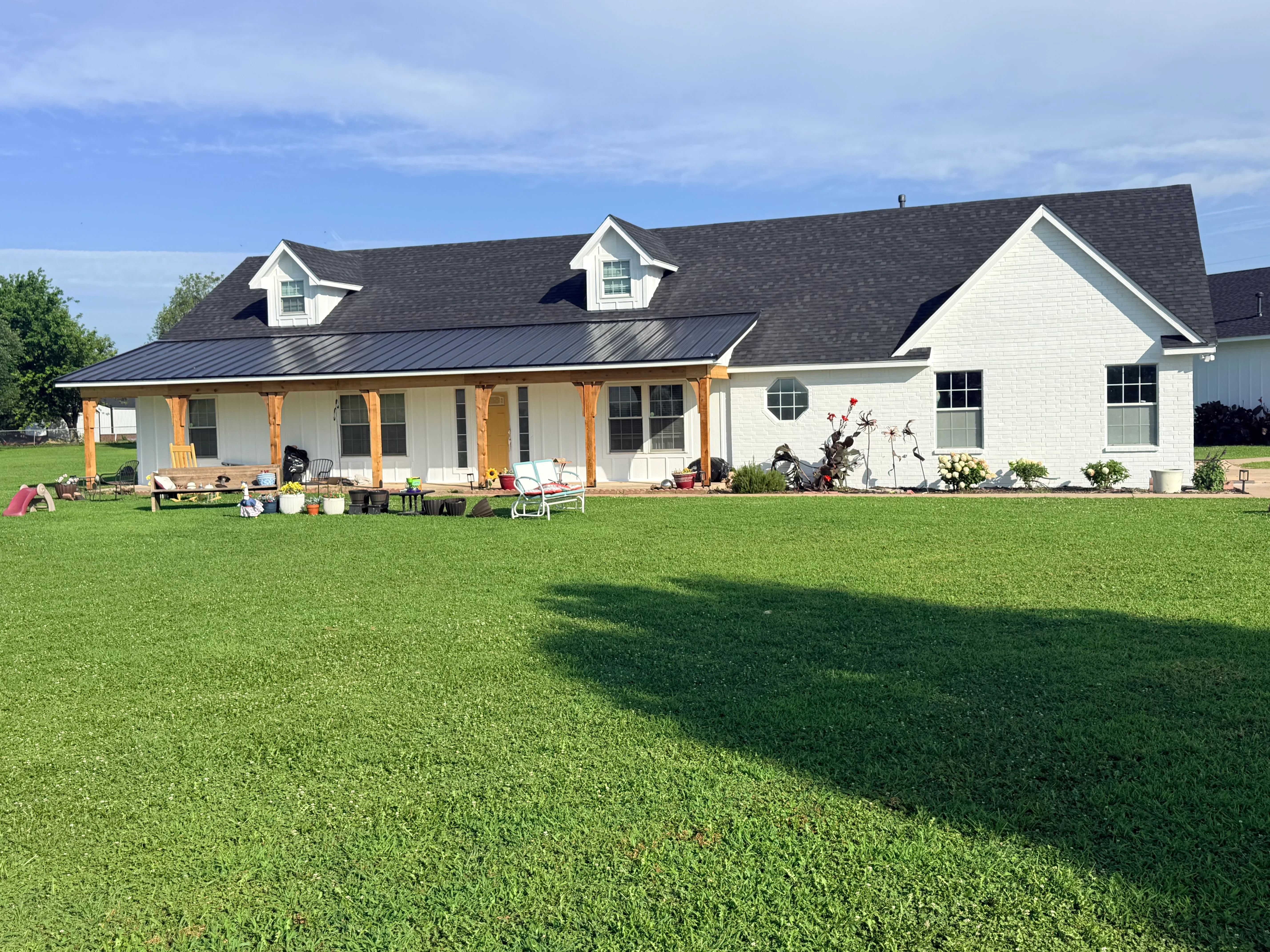 Charcoal gray architectural shingle roof with dormers on white brick farmhouse with metal porch roof