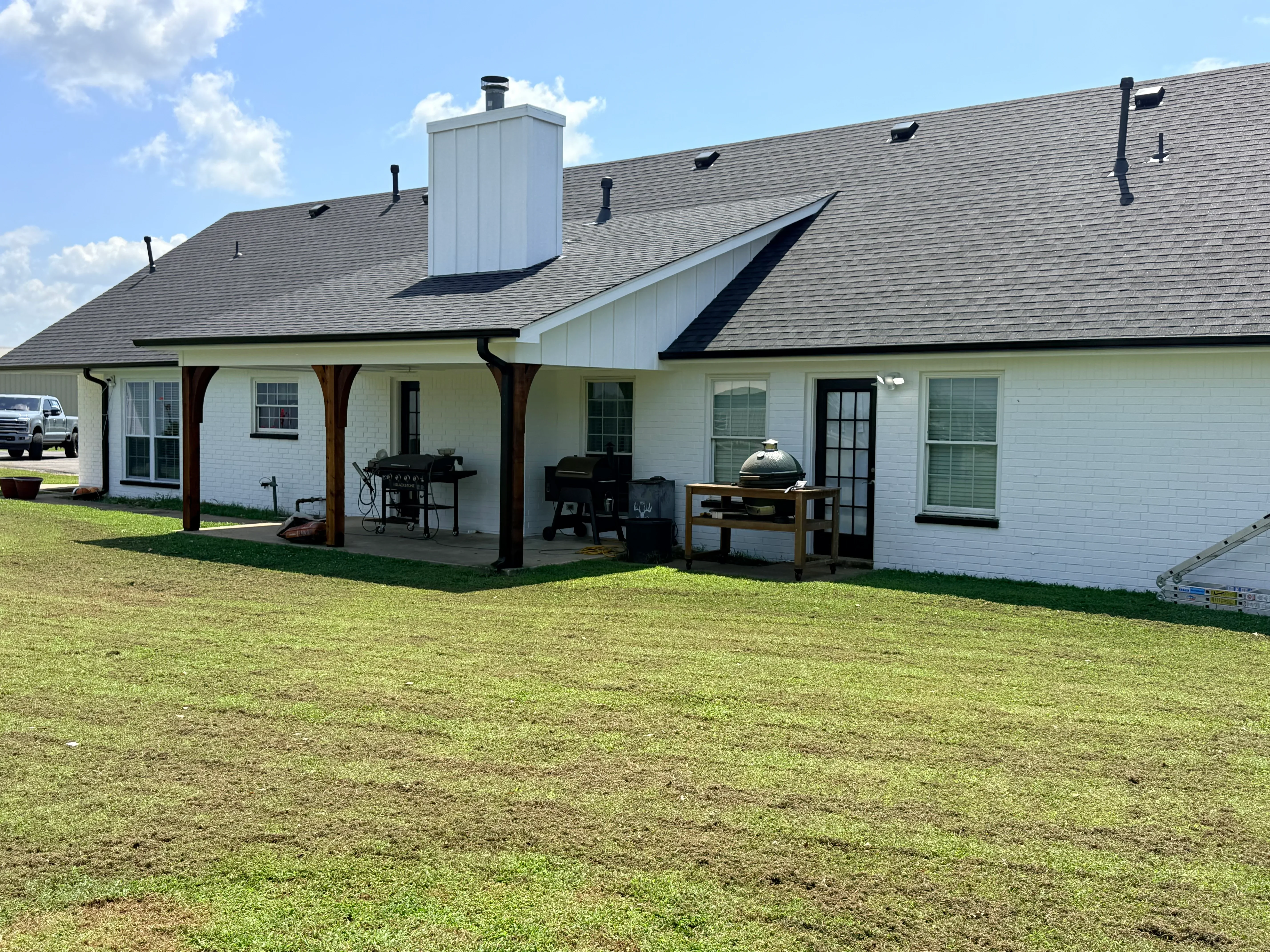 Gray architectural shingle roof with white chimney chase and black metal roof vents on brick home