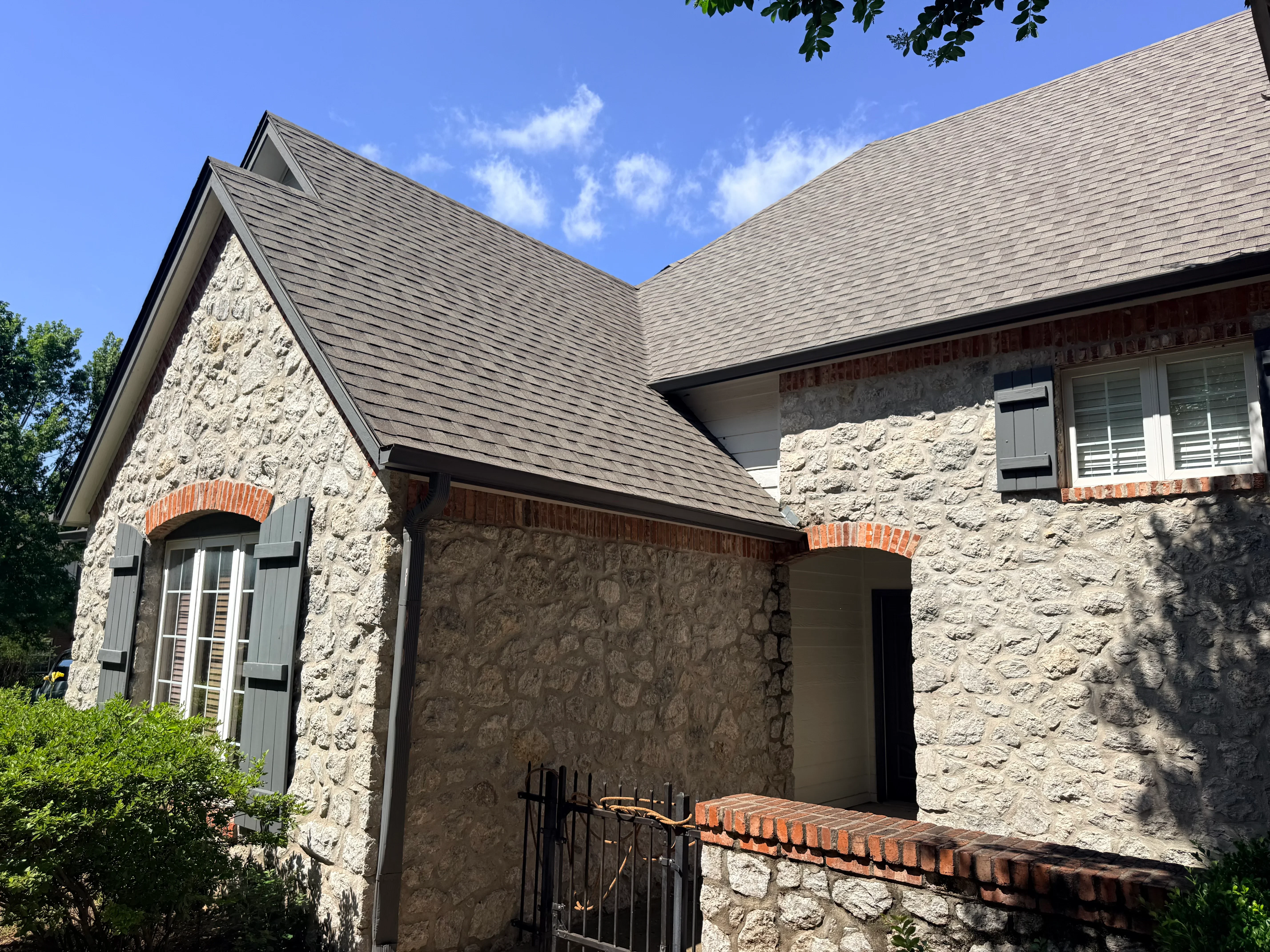 Gray architectural shingle roof installation on stone and brick home with multiple roof peaks