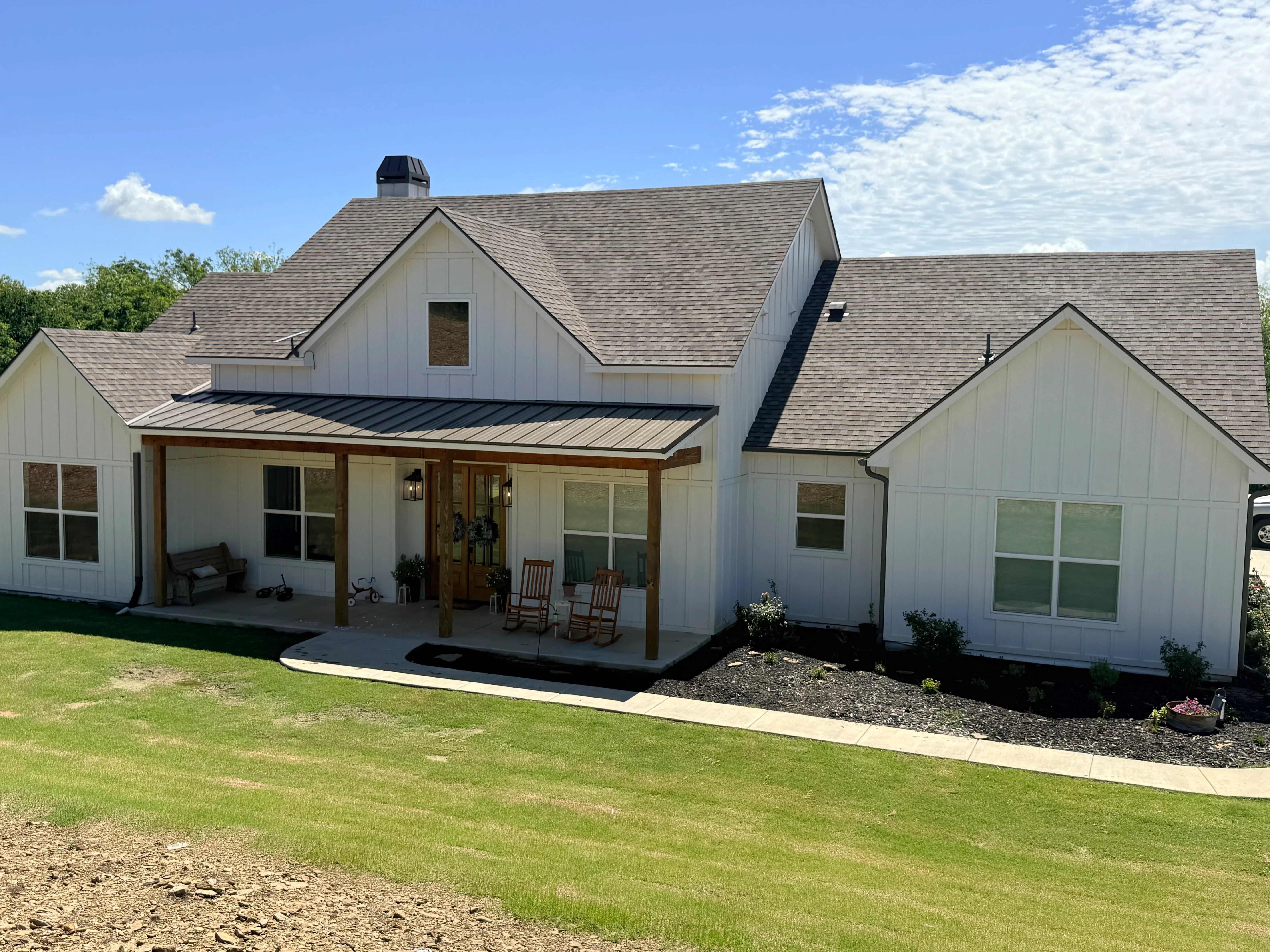 Gray architectural shingle roof with white siding and metal roof accents on farmhouse