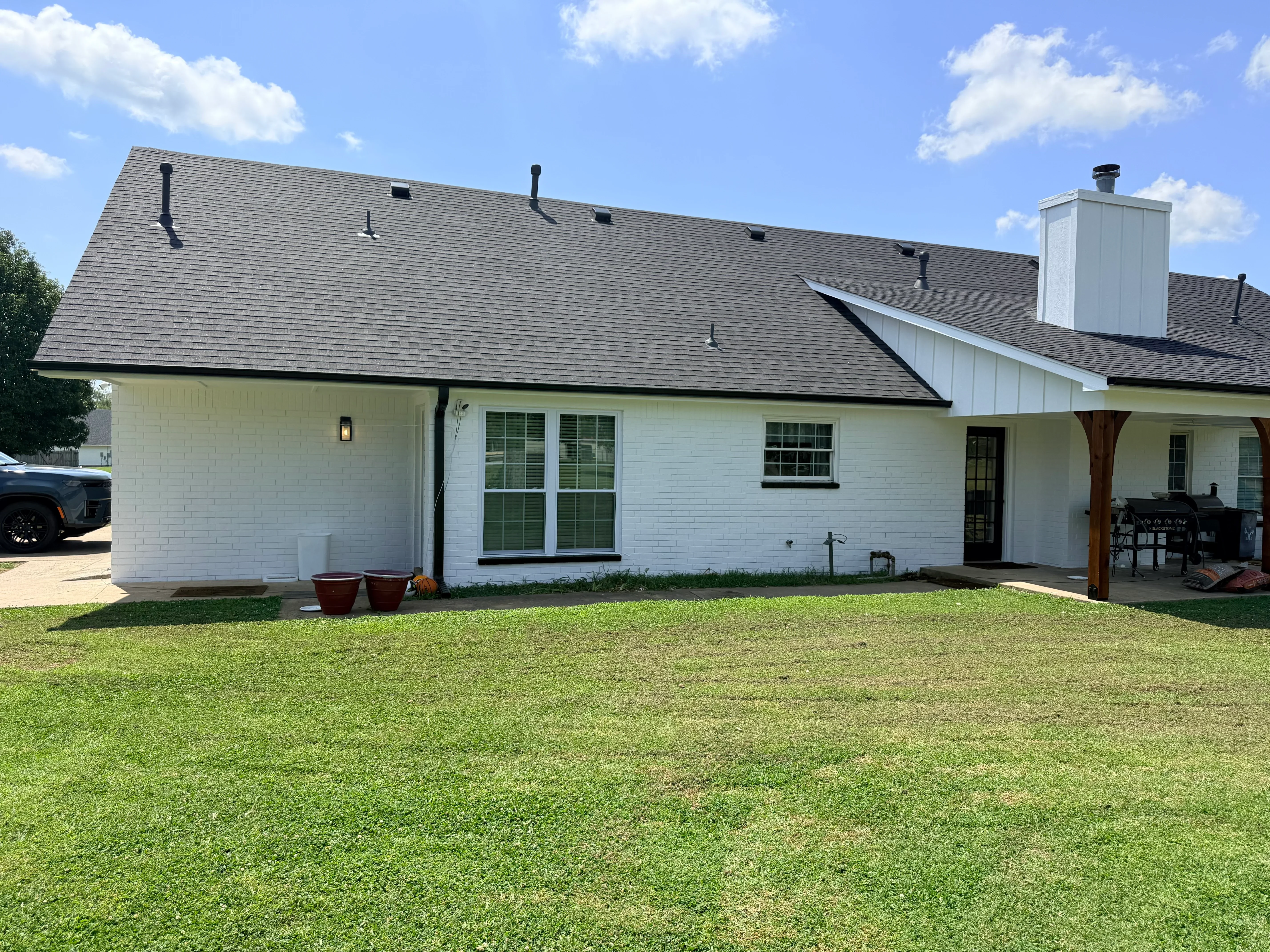 Gray architectural shingle roof with white metal chimney on modern farmhouse with white brick siding