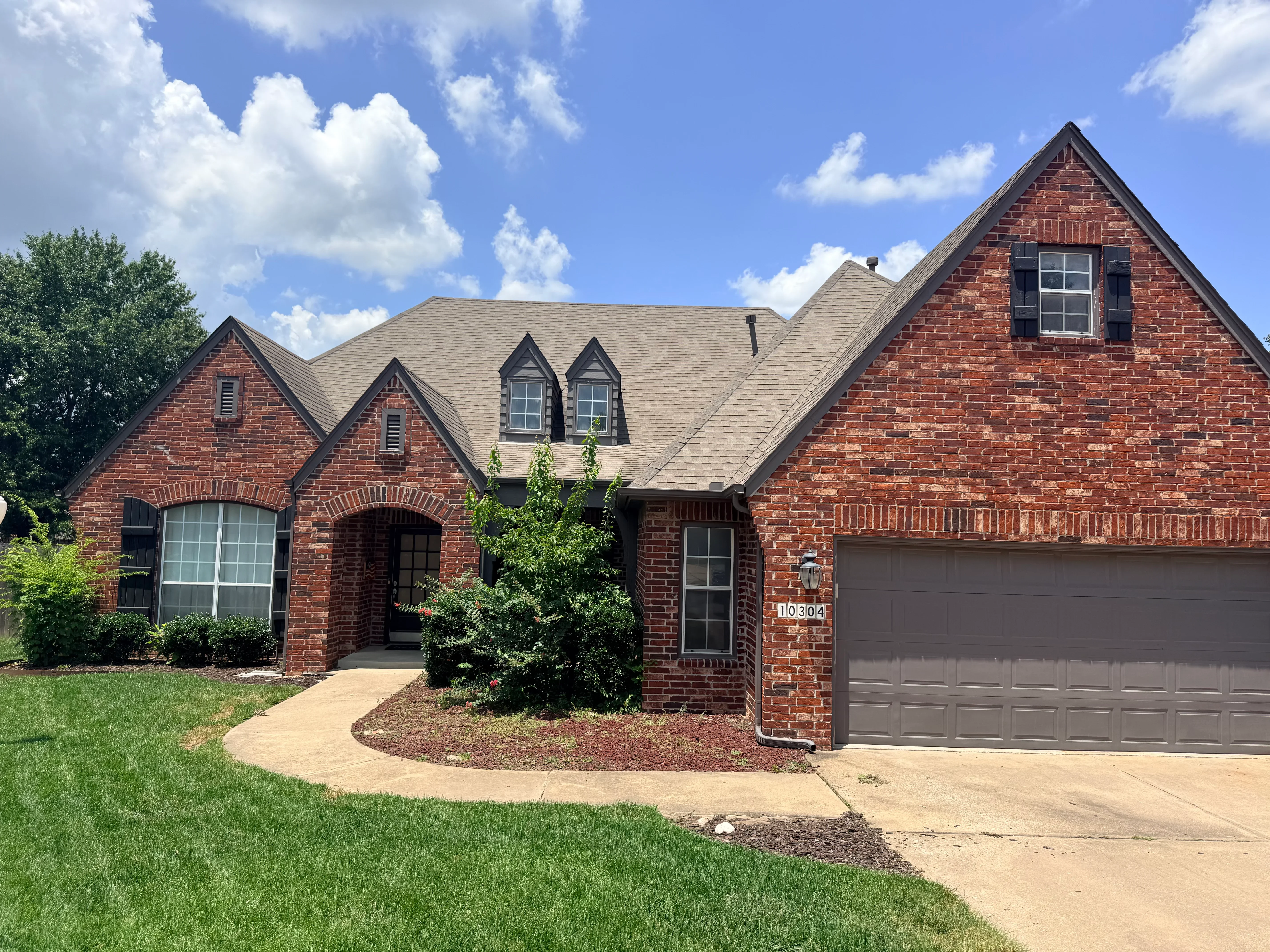 Two-story brick home with new gray asphalt shingle roof installation, multiple gables and dormers