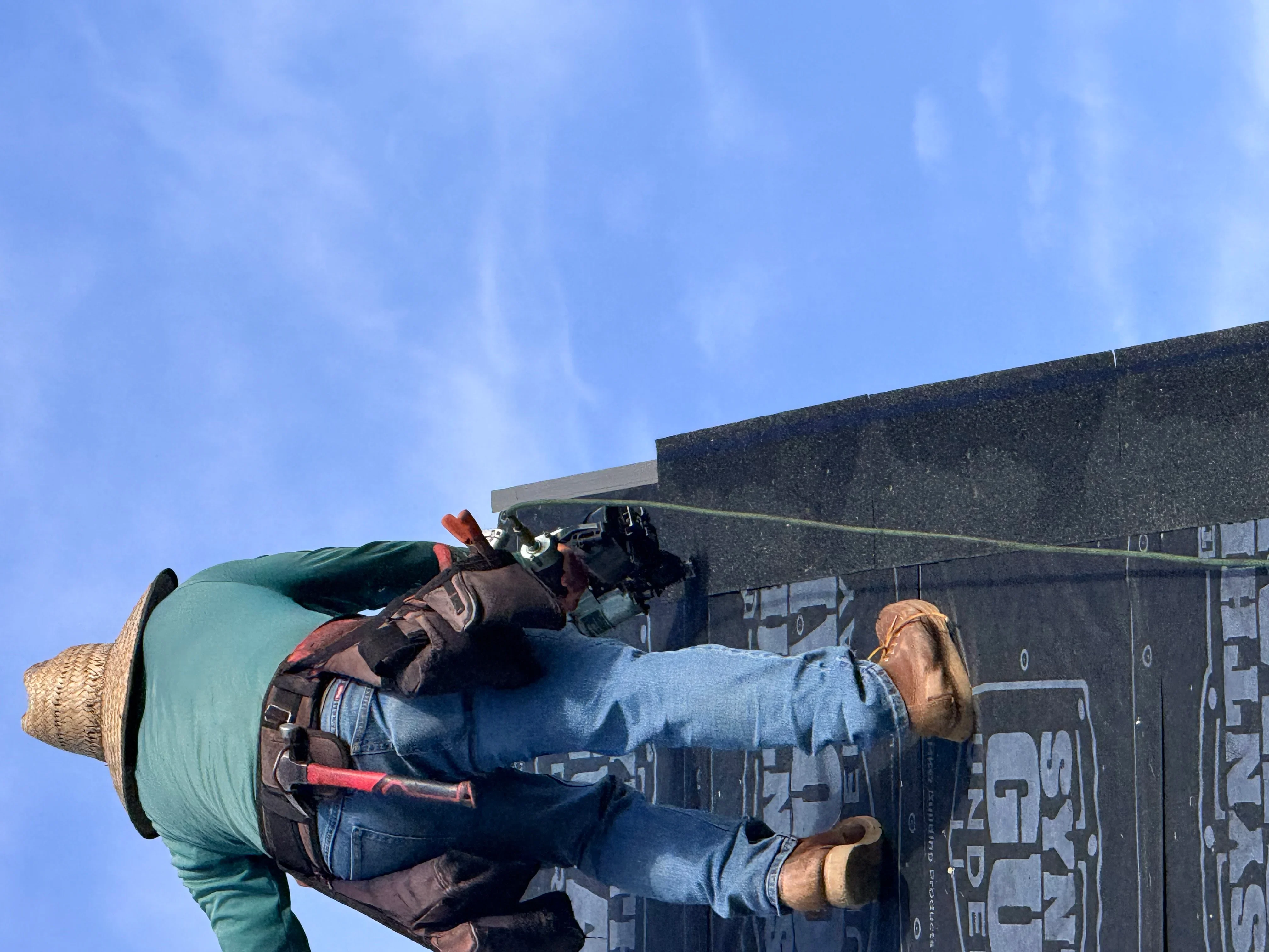Roofer installing asphalt shingles on pitched residential roof with safety harness