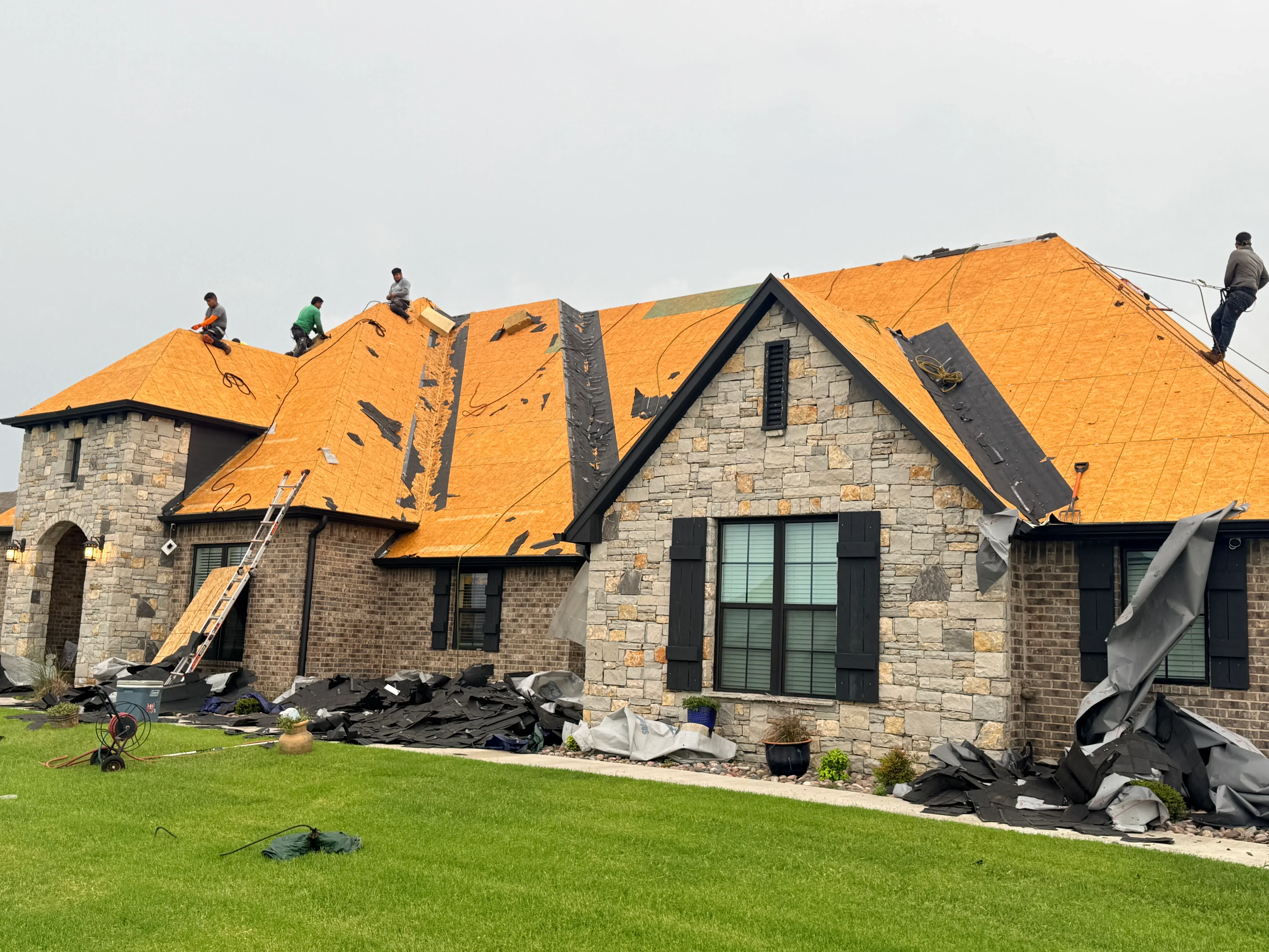 Golden orange architectural shingles installed on multi-gabled stone home roof during replacement project