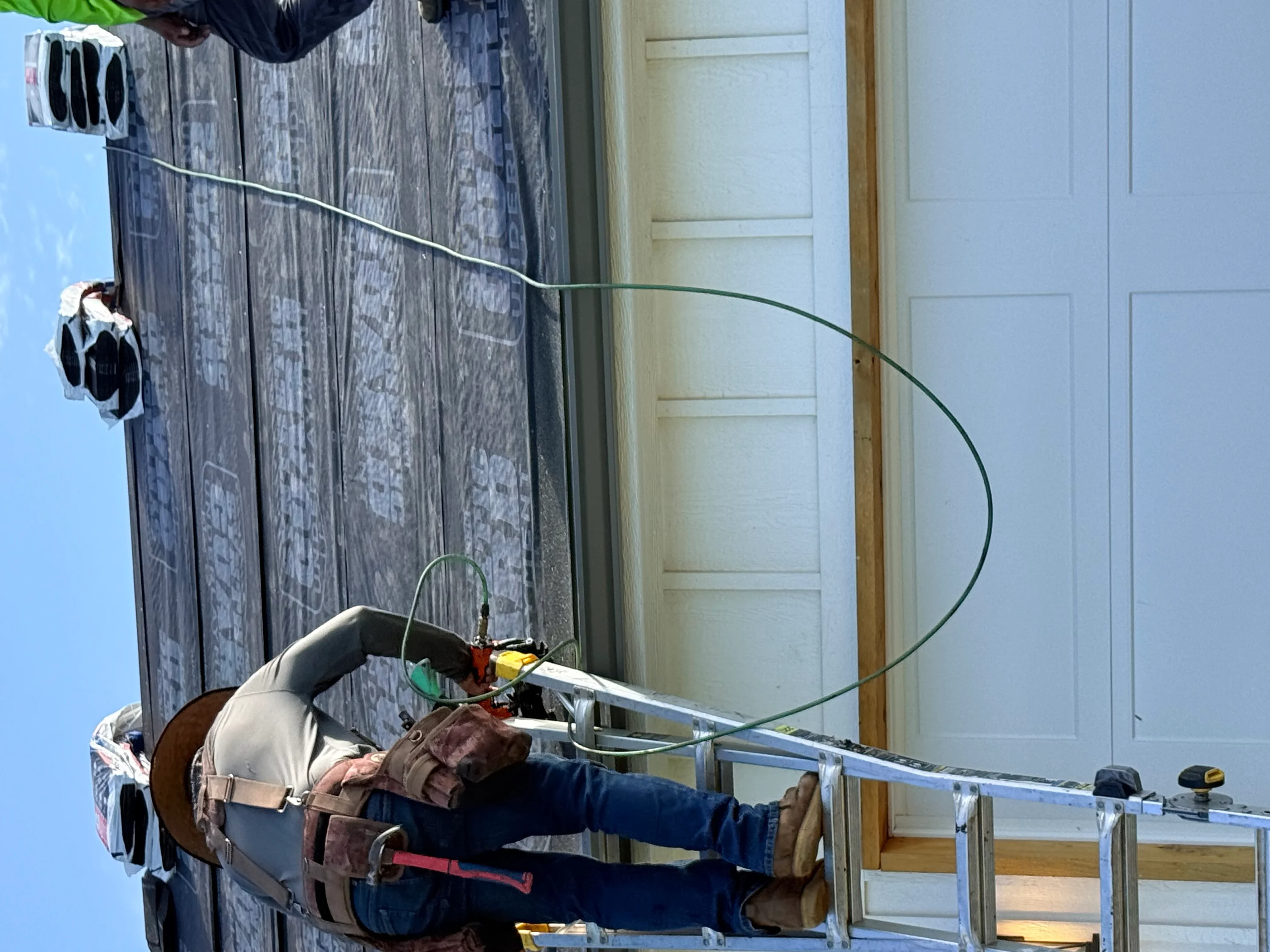 Roofer installing asphalt shingles on pitched residential roof with safety harness