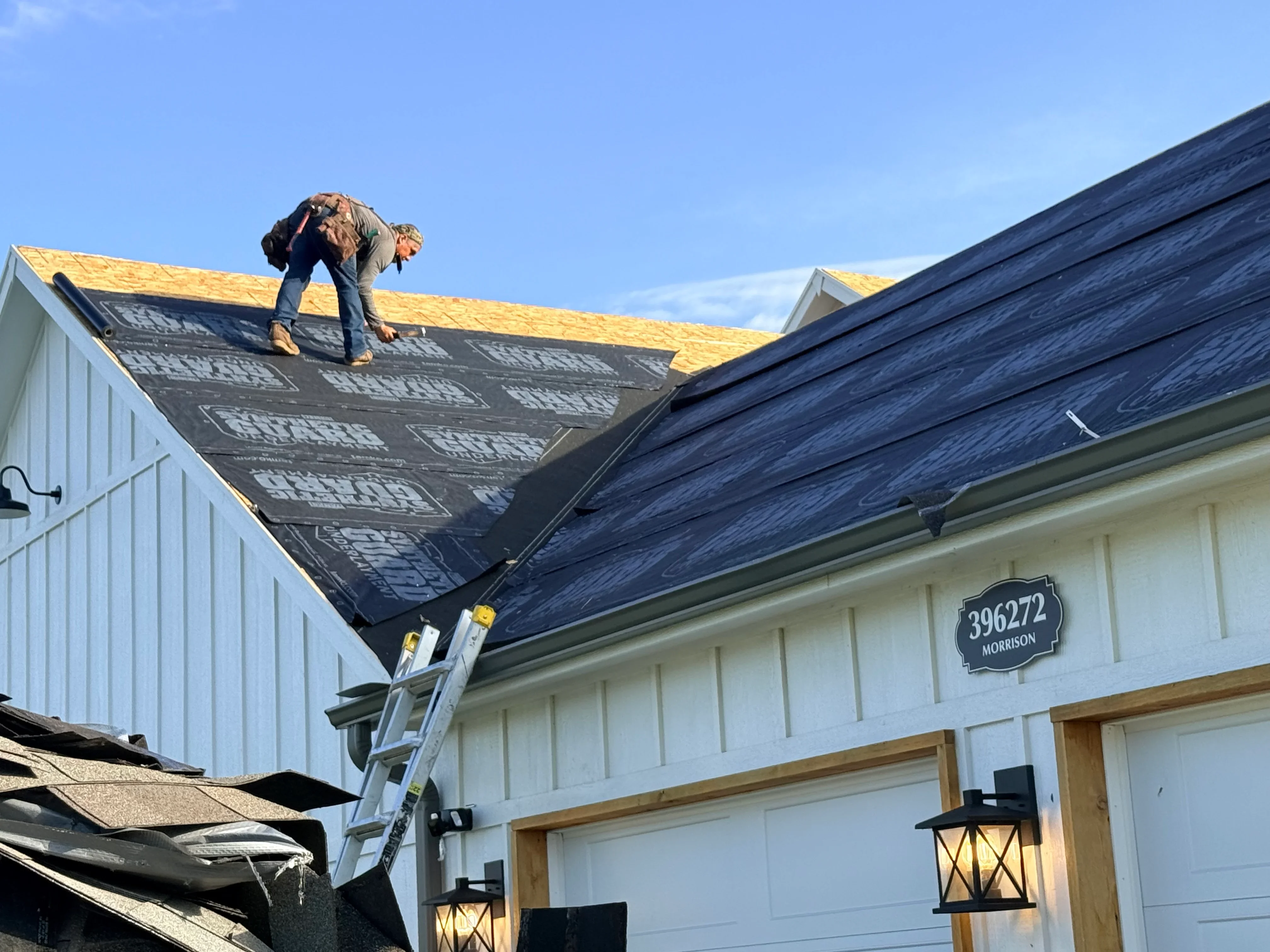 Roofer installing dark gray architectural shingles on residential home with yellow underlayment visible