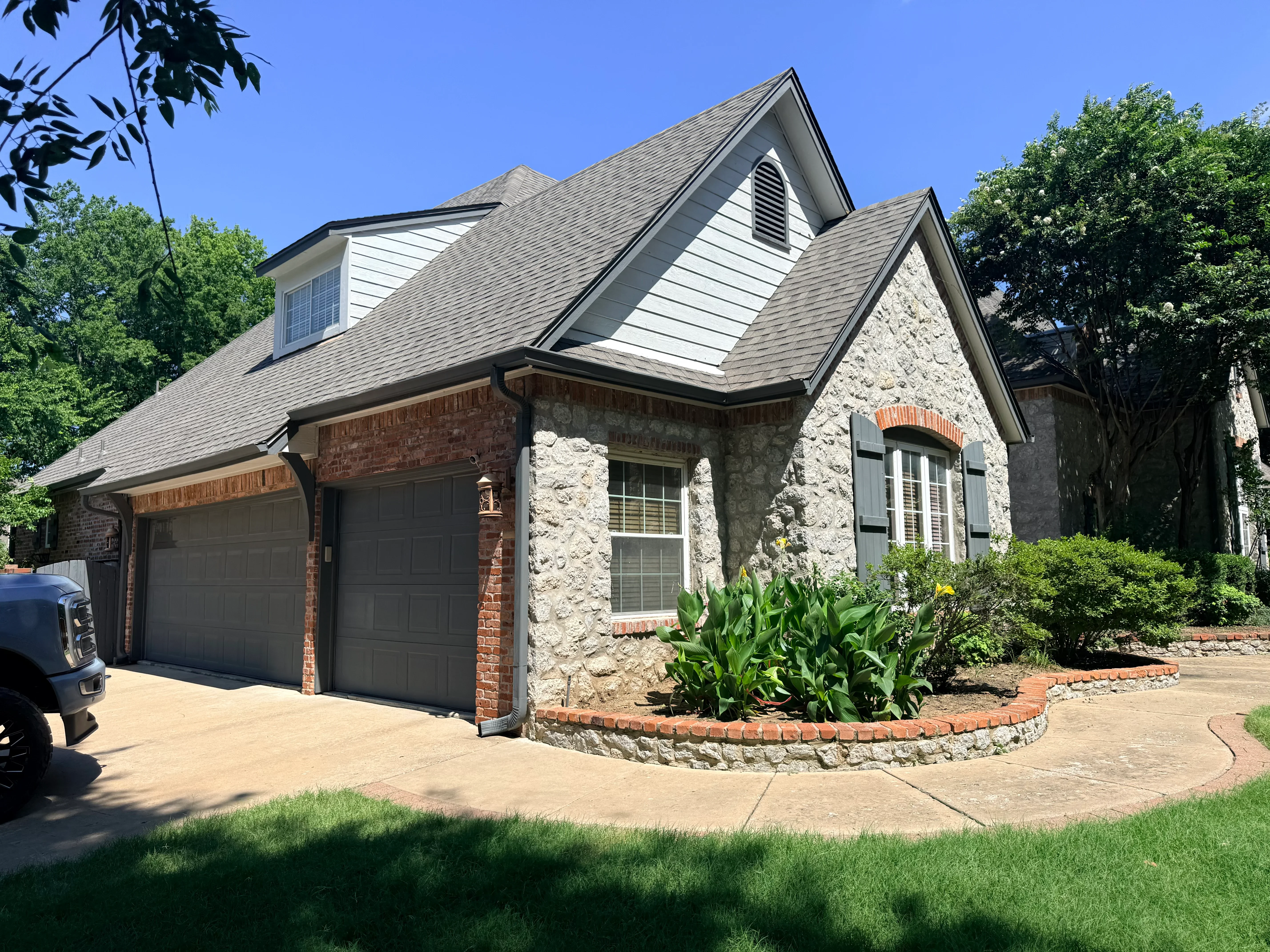 Gray architectural shingle roof on two-story home with stone and brick exterior, multiple roof planes and dormers