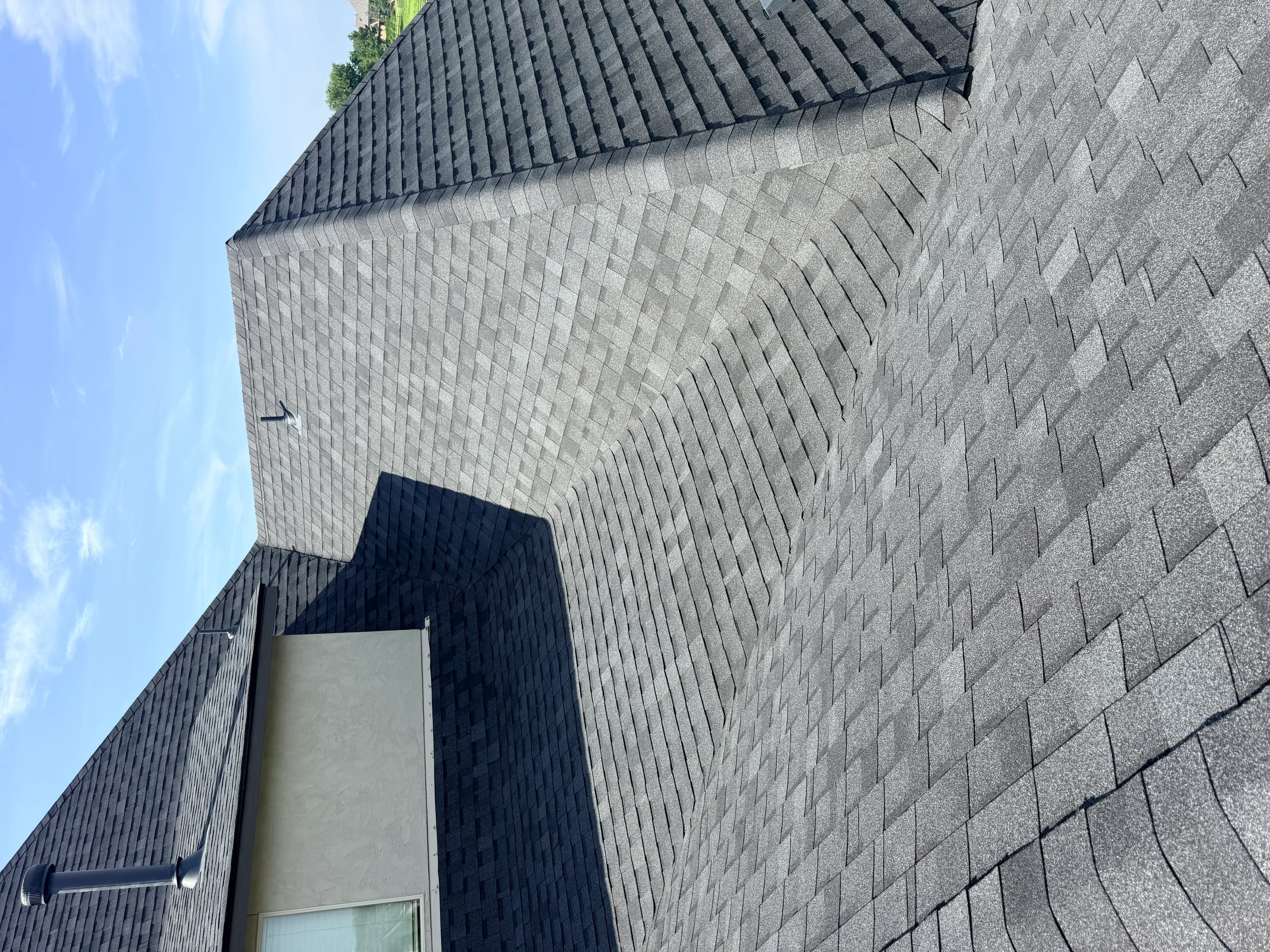 Charcoal gray architectural shingles installed on curved roofline with proper flashing