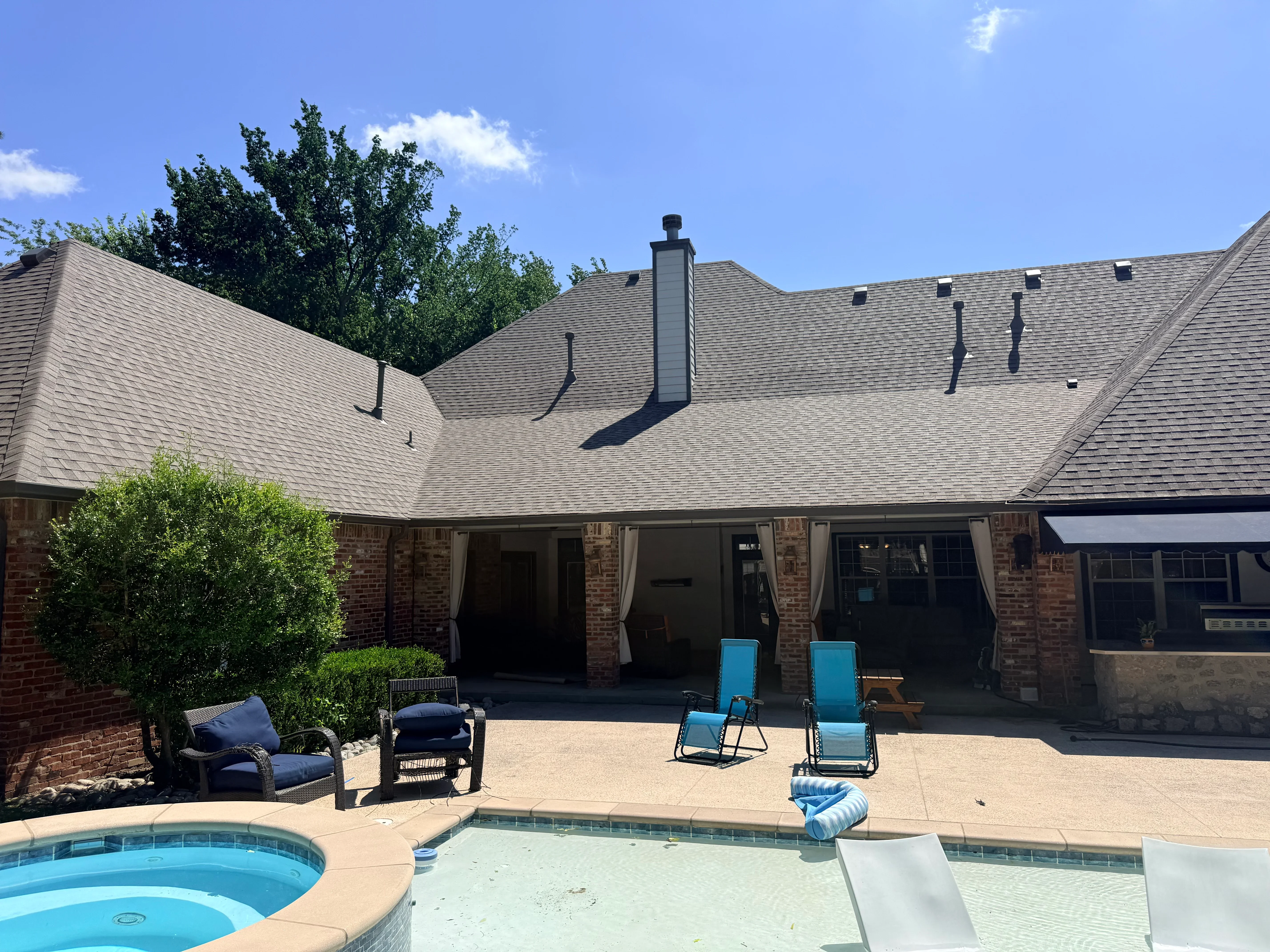 Gray architectural shingle roof with chimney flashing on brick home with pool patio