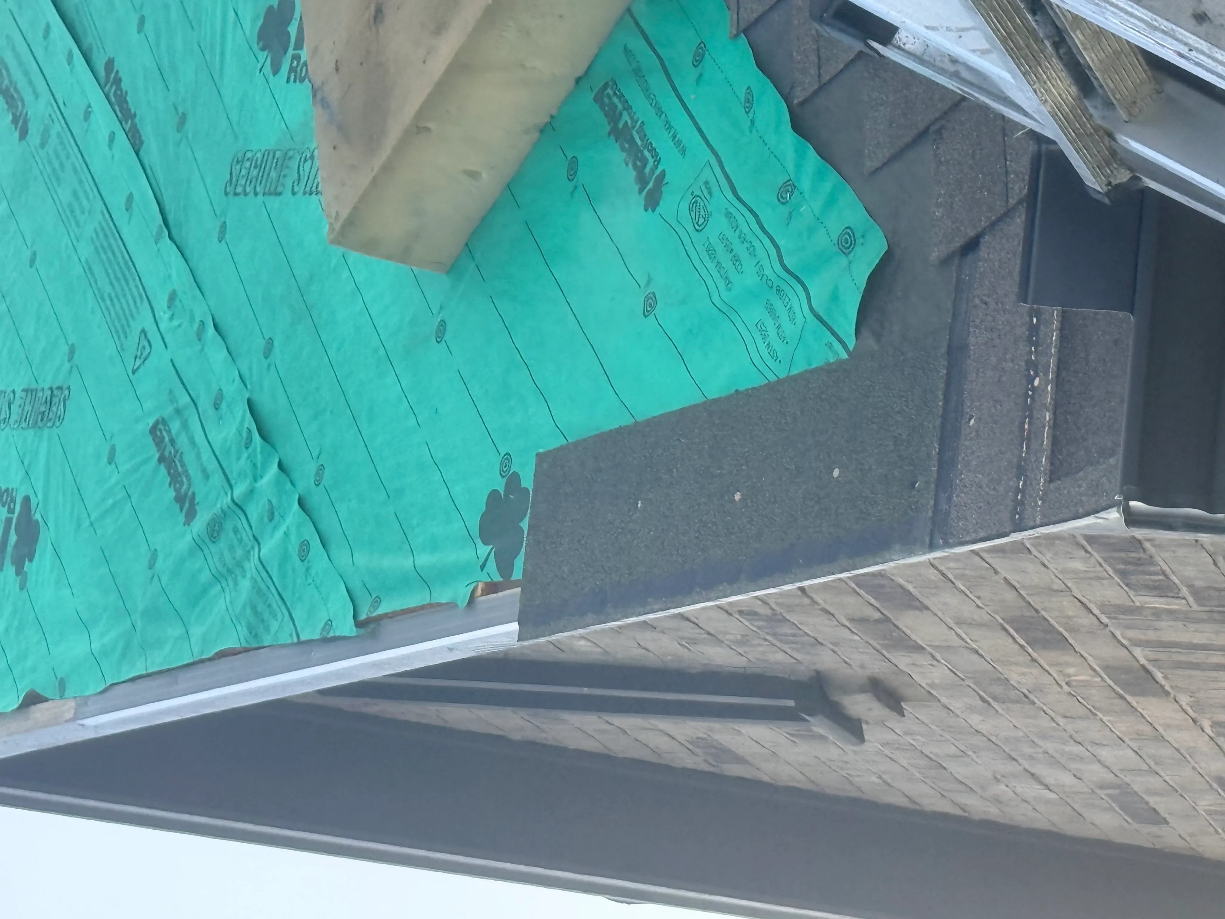 Turquoise synthetic roof underlayment installed over wood sheathing with metal flashing and drip edge