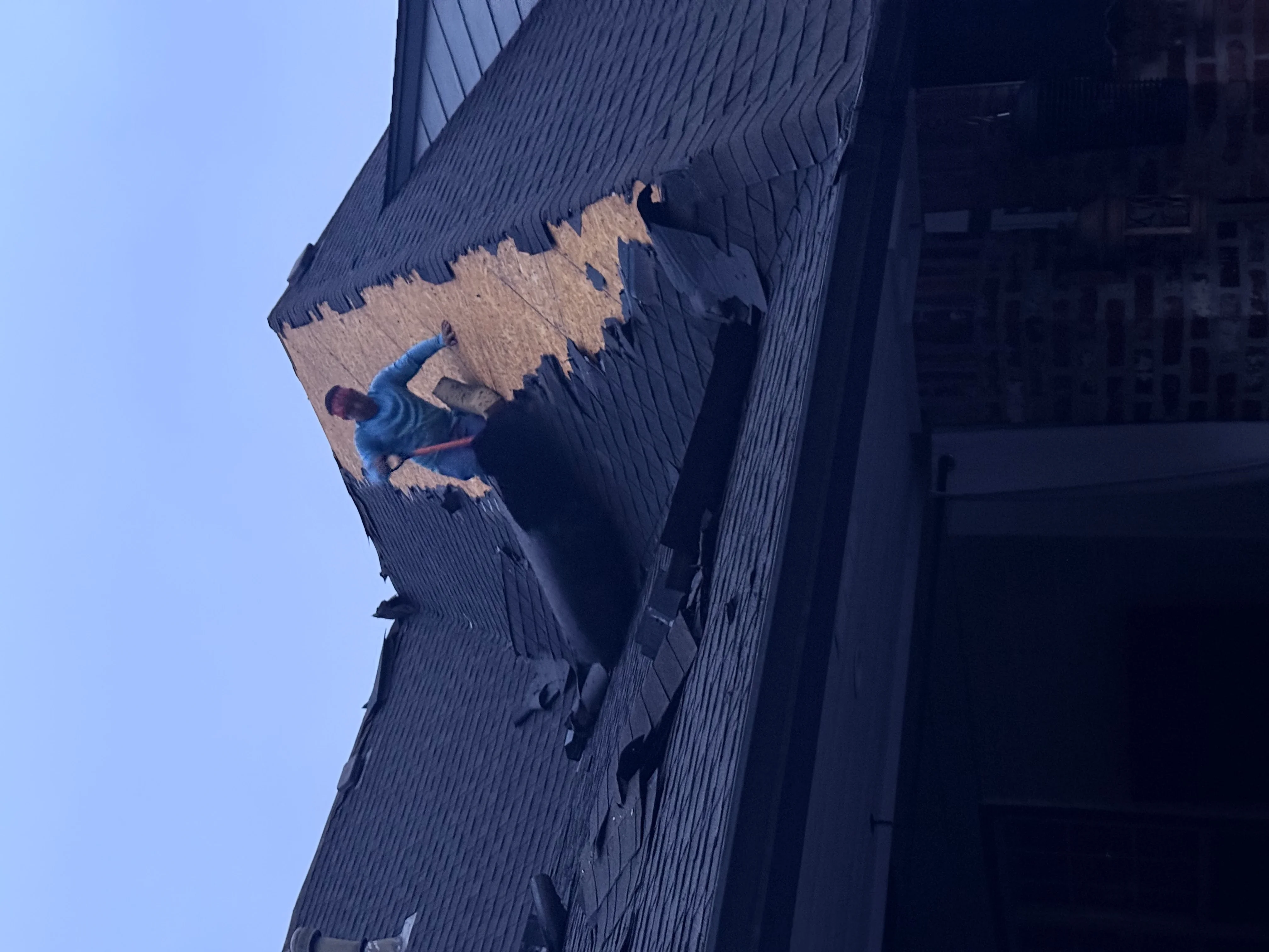Worker installing new corrugated metal roofing panels over damaged section of roof