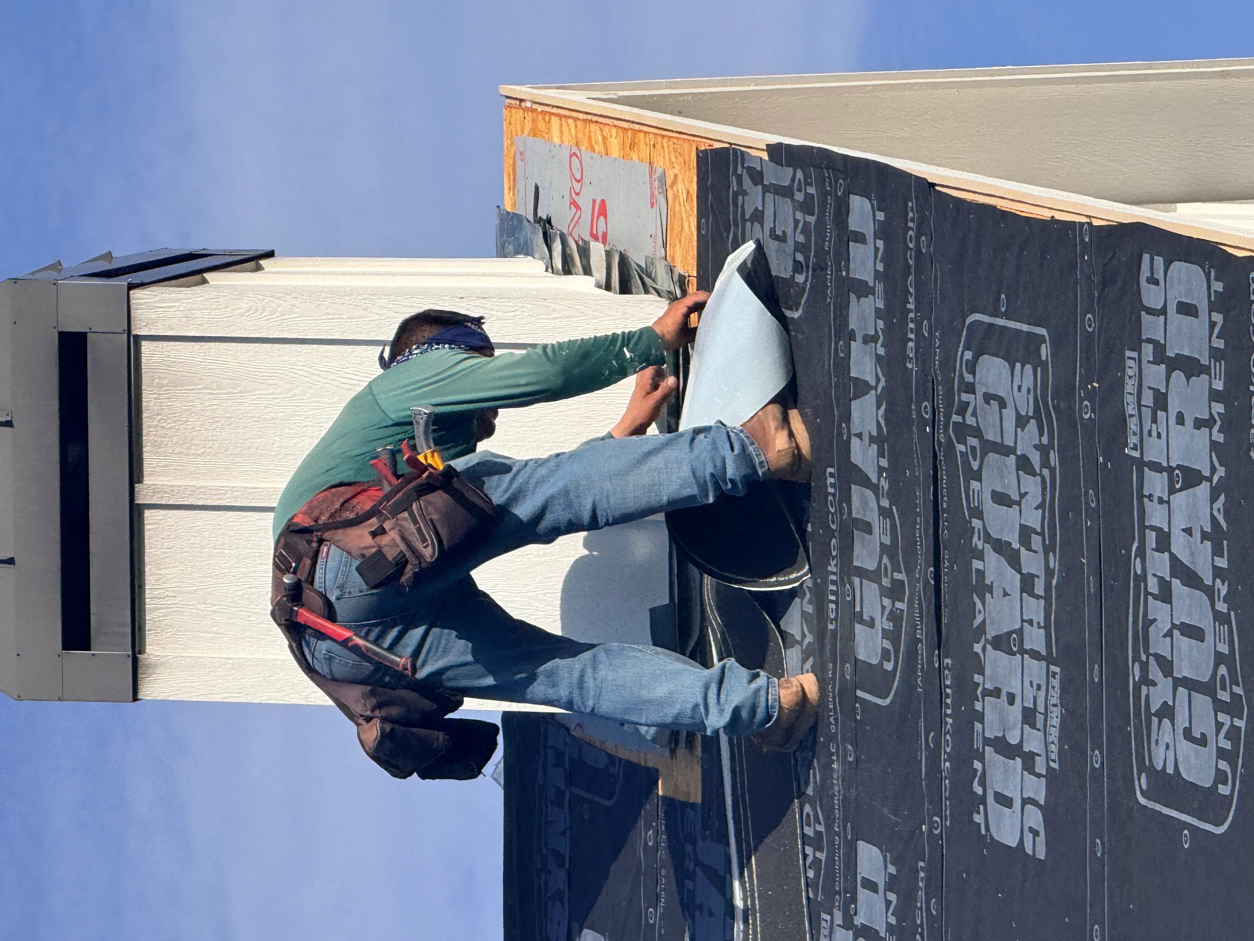 Worker installing black roofing underlayment and weather barrier on roof sheathing