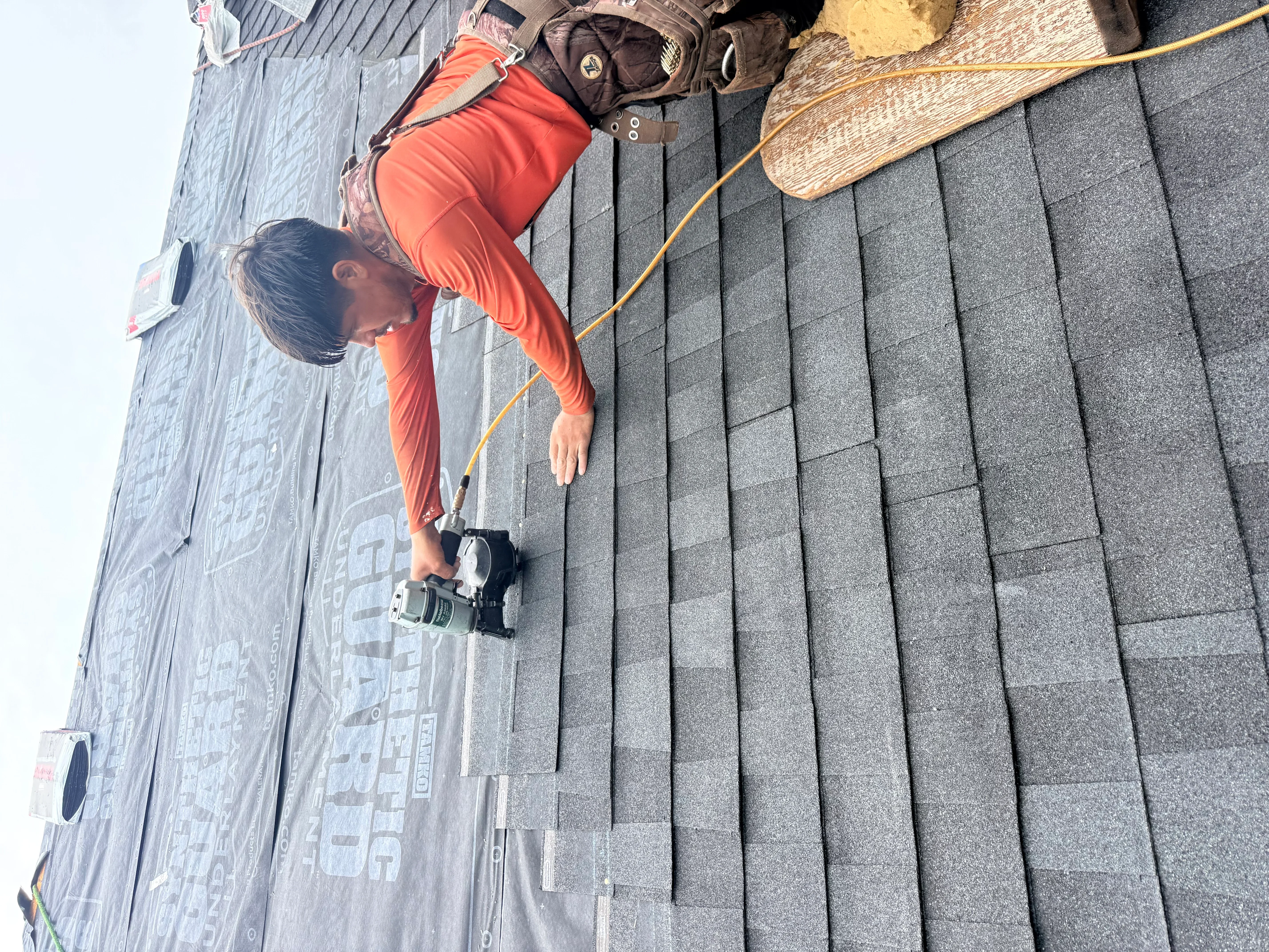 Roofer installing charcoal gray architectural shingles on pitched roof with proper underlayment