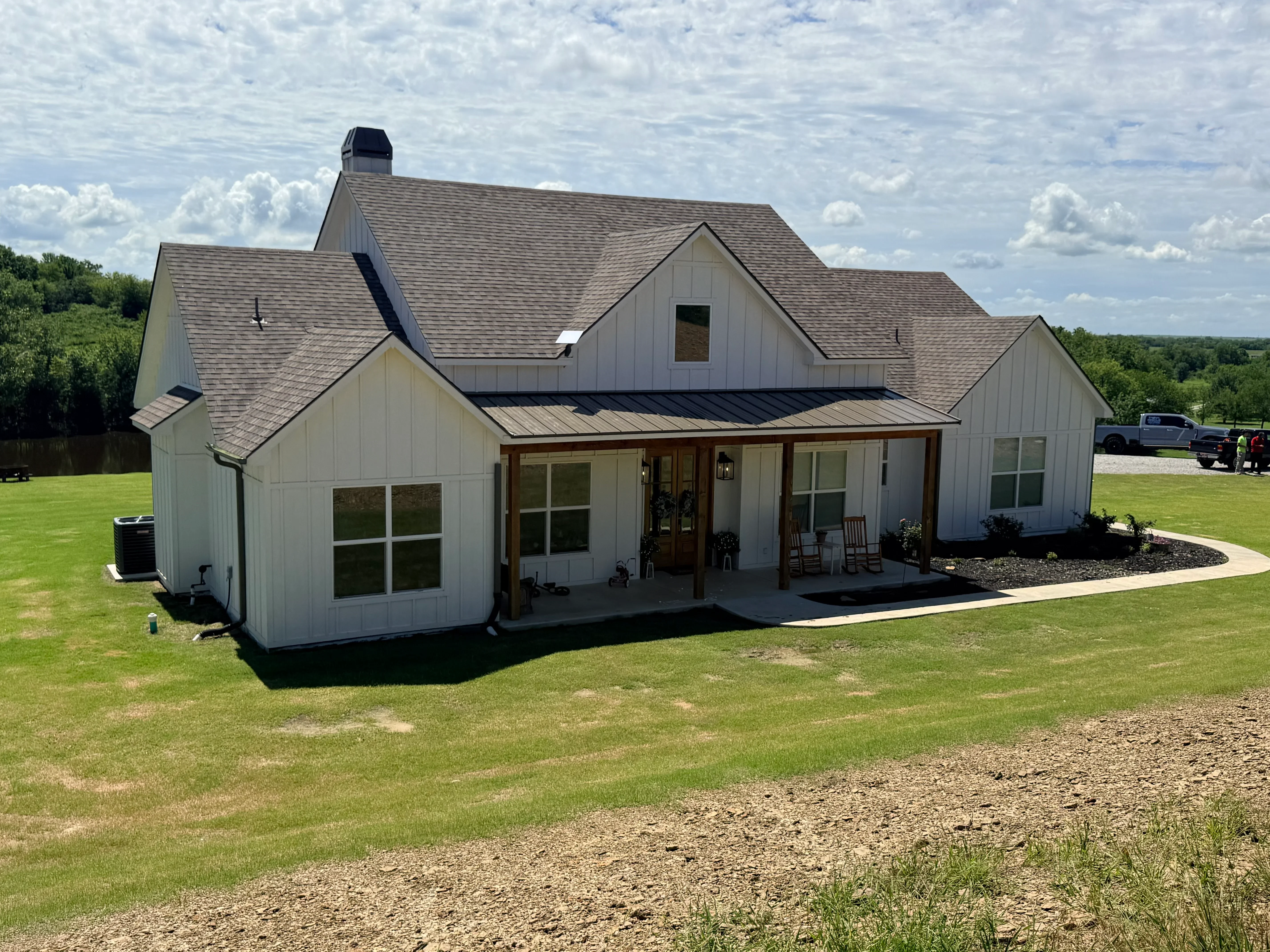 Gray architectural shingles and metal roof on multi-gable farmhouse with white siding