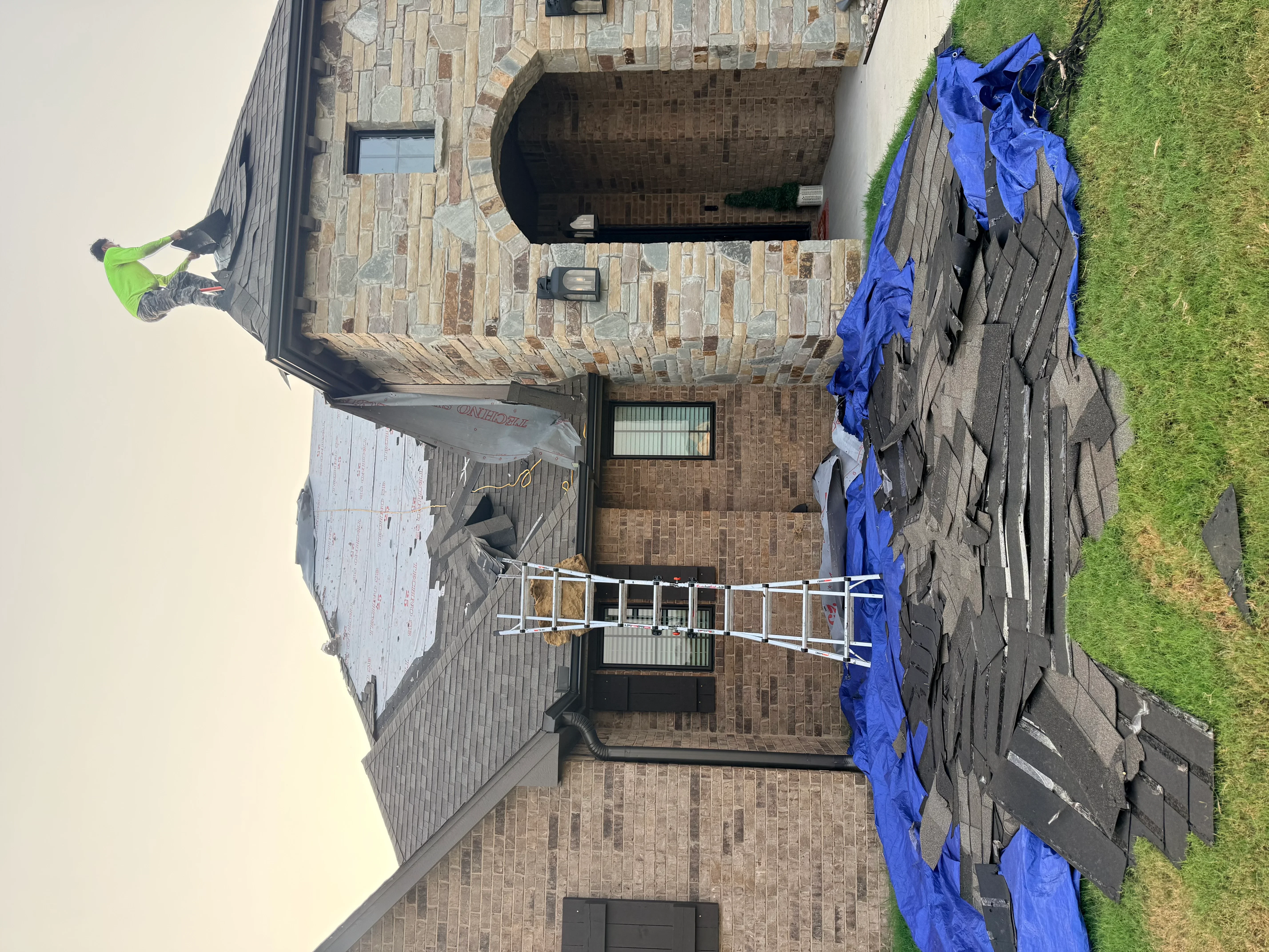 Roof replacement in progress with blue tarps protecting brick home and surrounding areas