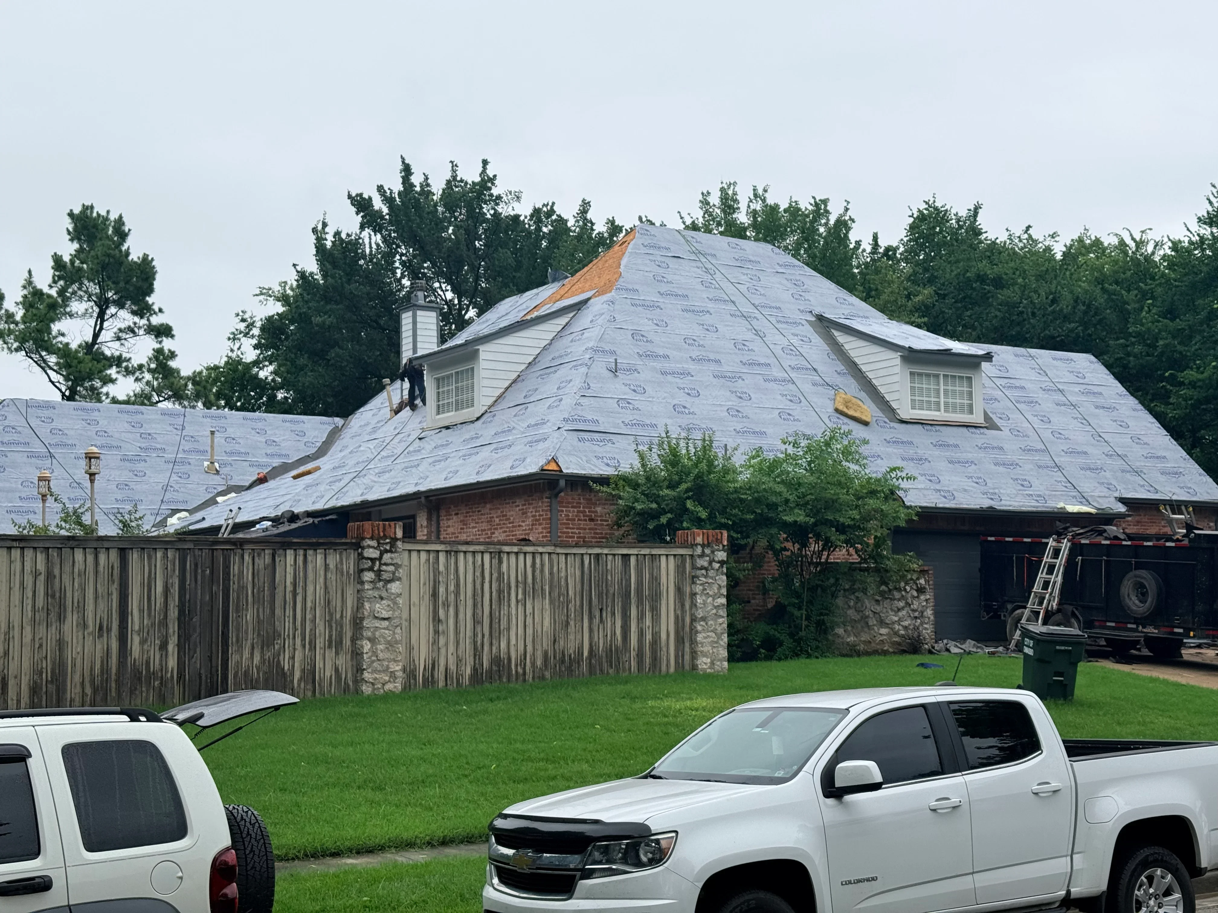 Brick home with new roof underlayment and dormers during installation, white trim and siding visible