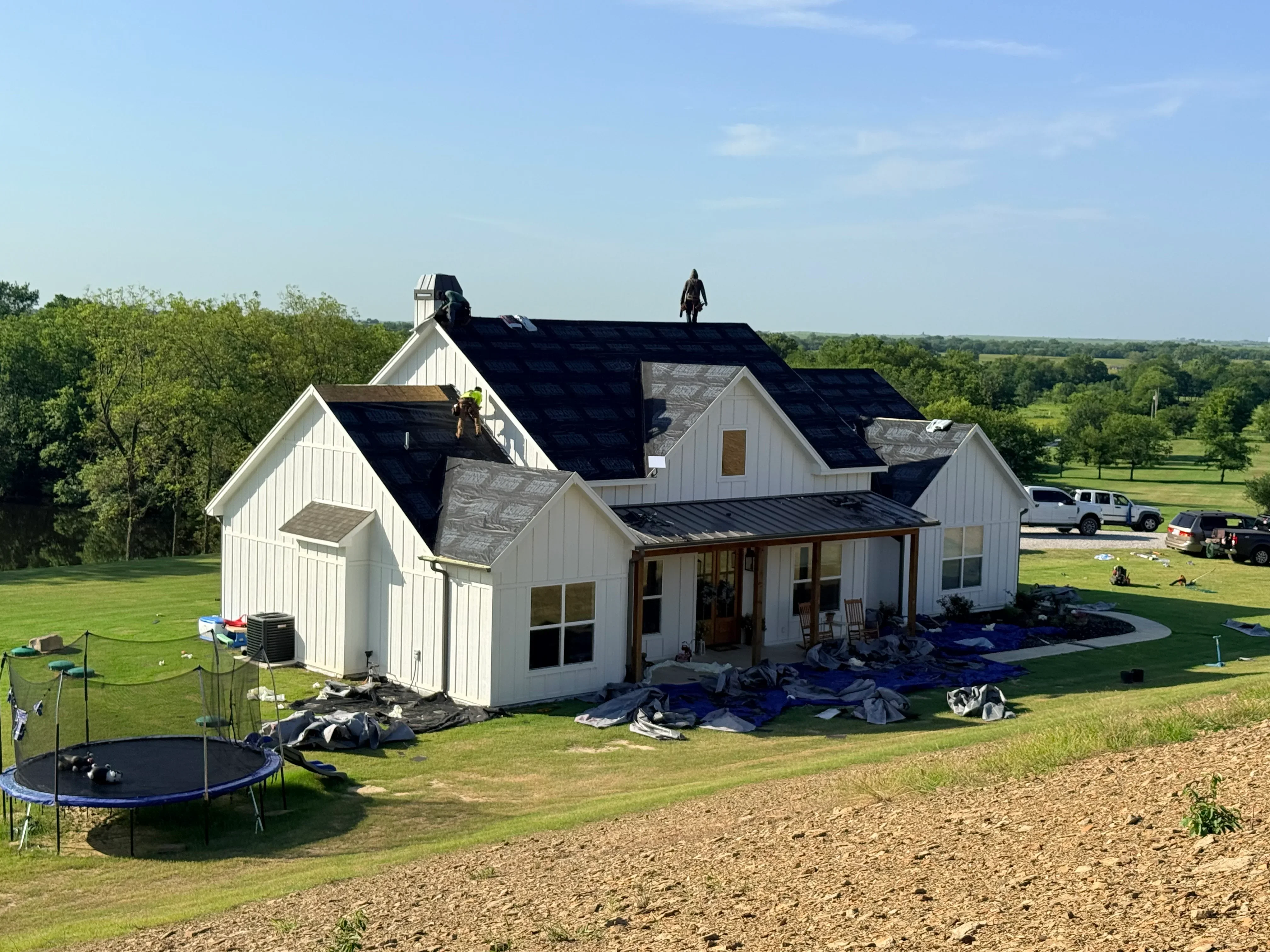 New dark asphalt shingle roof on white farmhouse with multiple gables and dormers