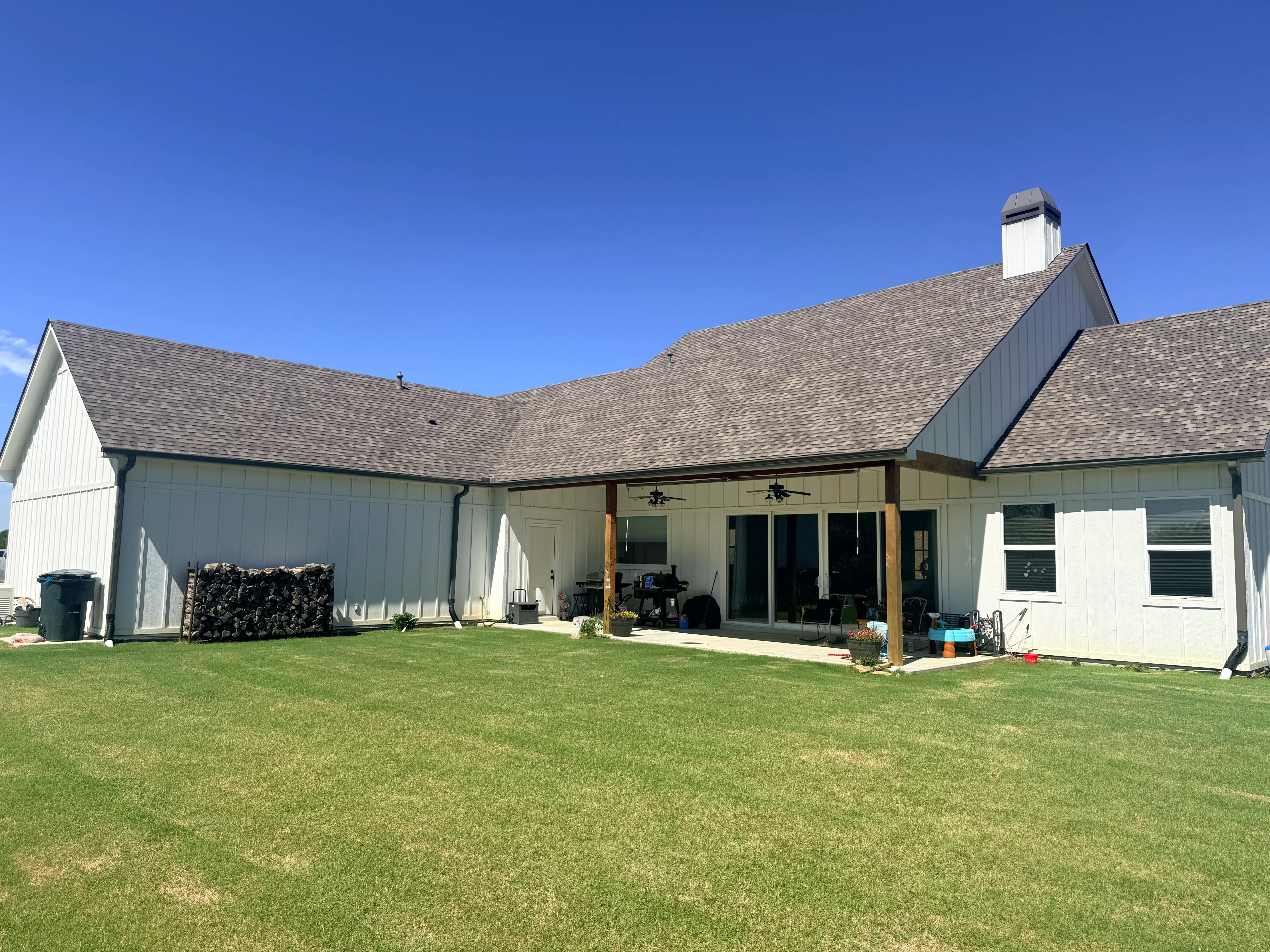 Gray architectural shingle roof on white farmhouse with covered porch and metal accents