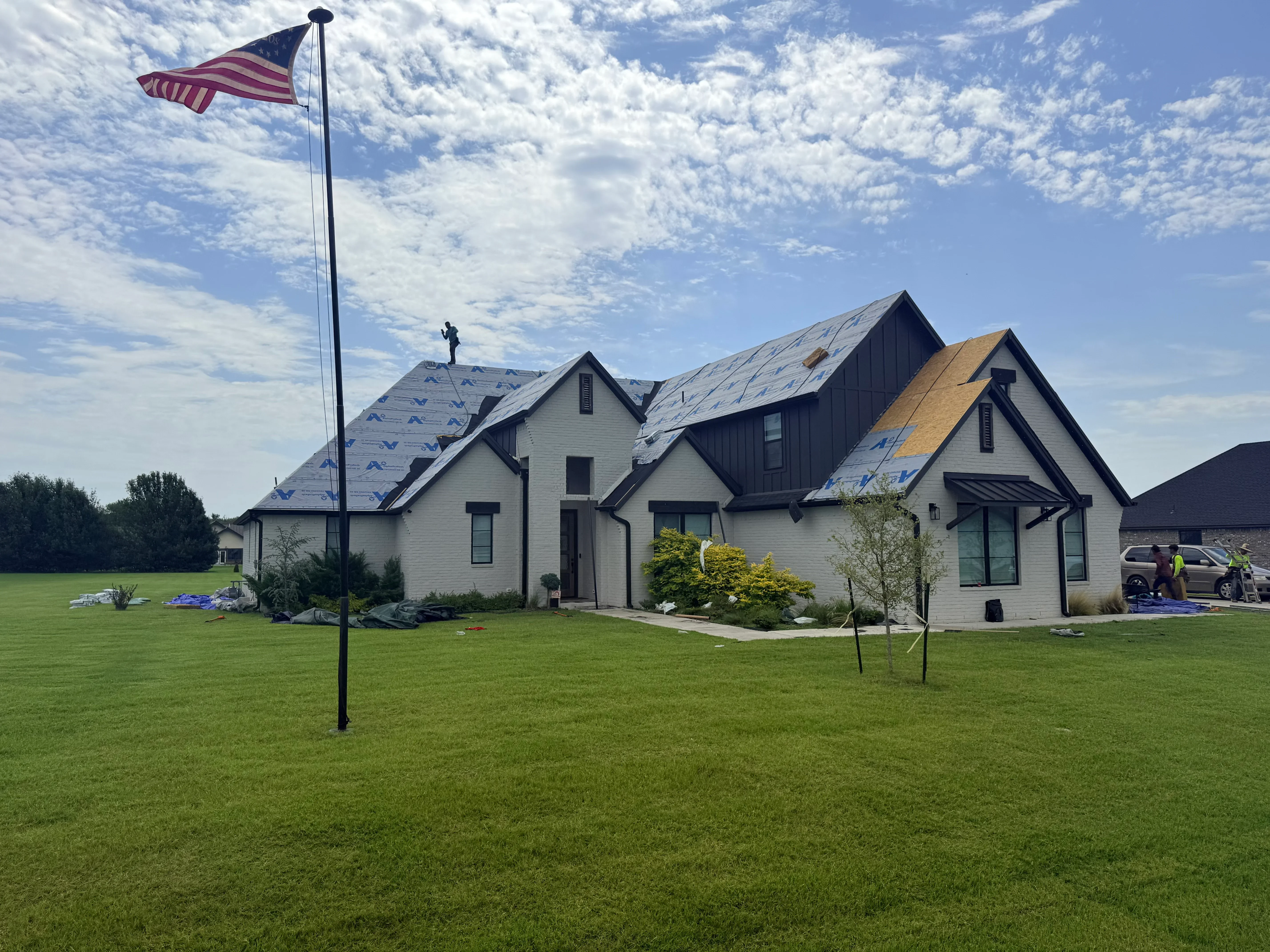Multi-gable farmhouse with newly installed gray and charcoal architectural shingles, white siding, and black trim