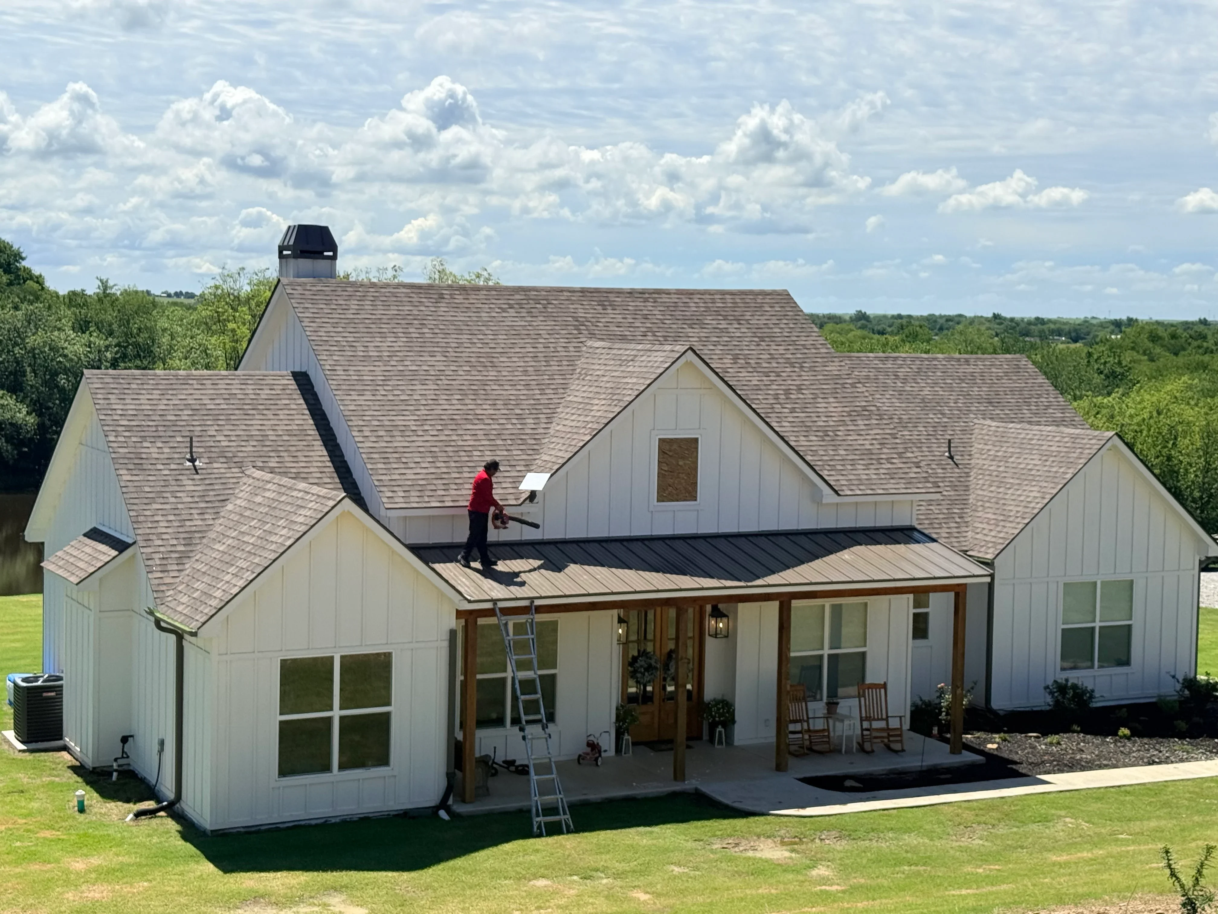 Farmhouse with dimensional shingle and standing seam metal roofing during installation