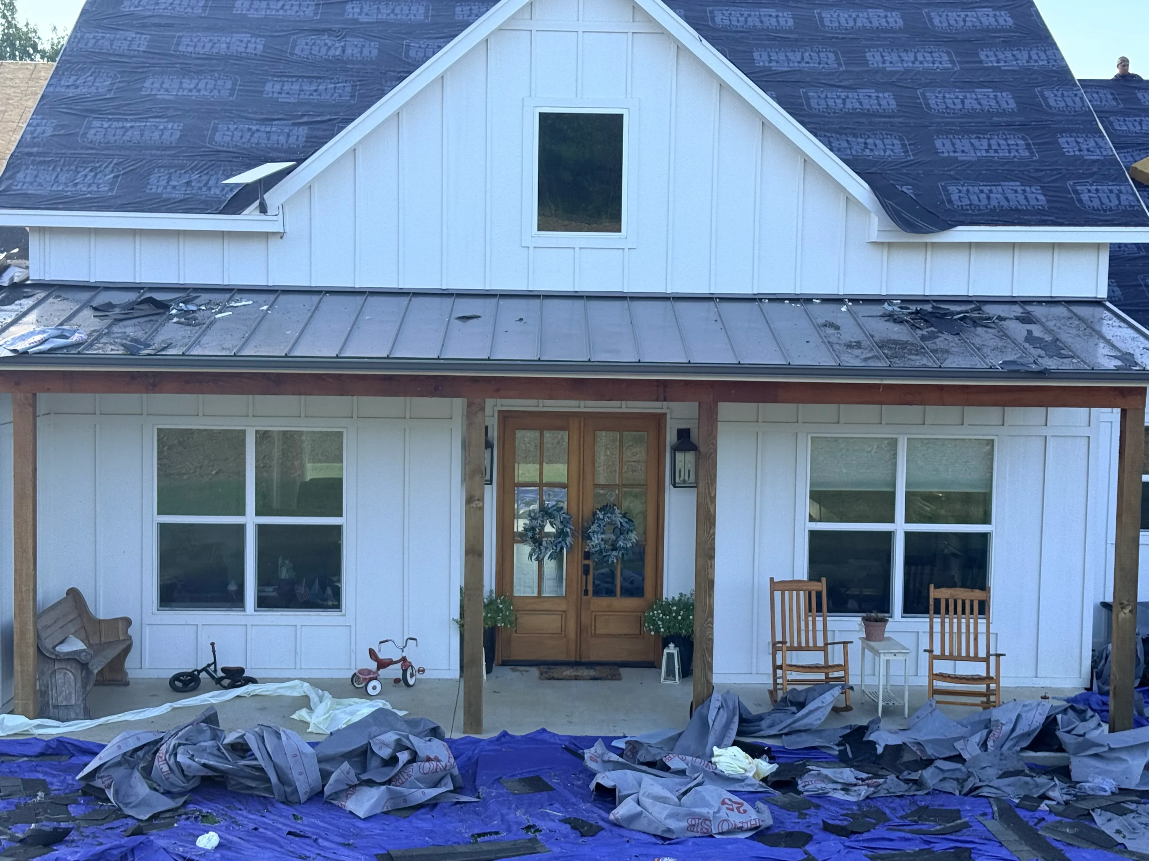 Standing seam metal roof installation on white farmhouse with gable dormers and wood trim