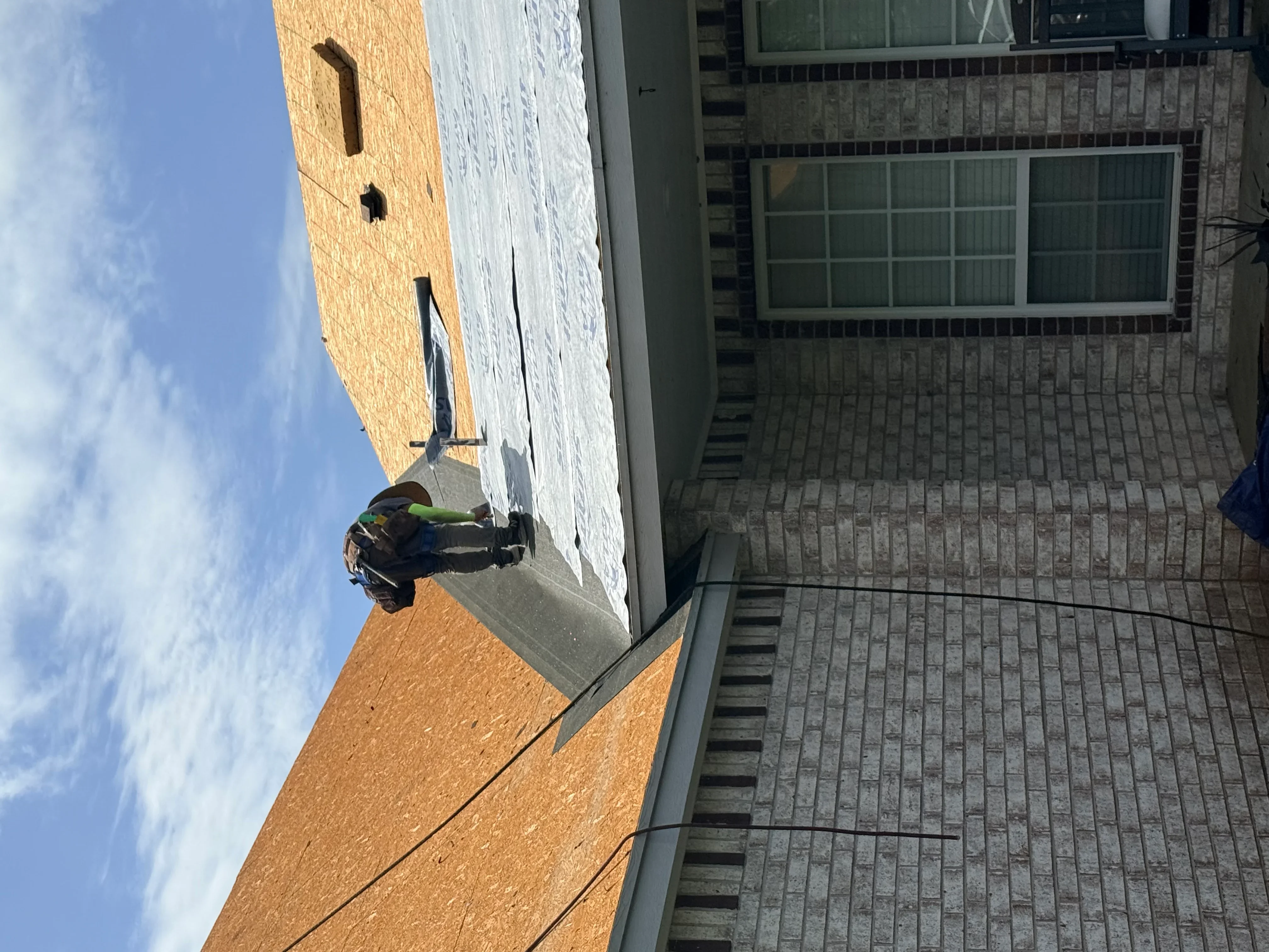 Roofer installing architectural shingles on residential roof with brick chimney and gable details