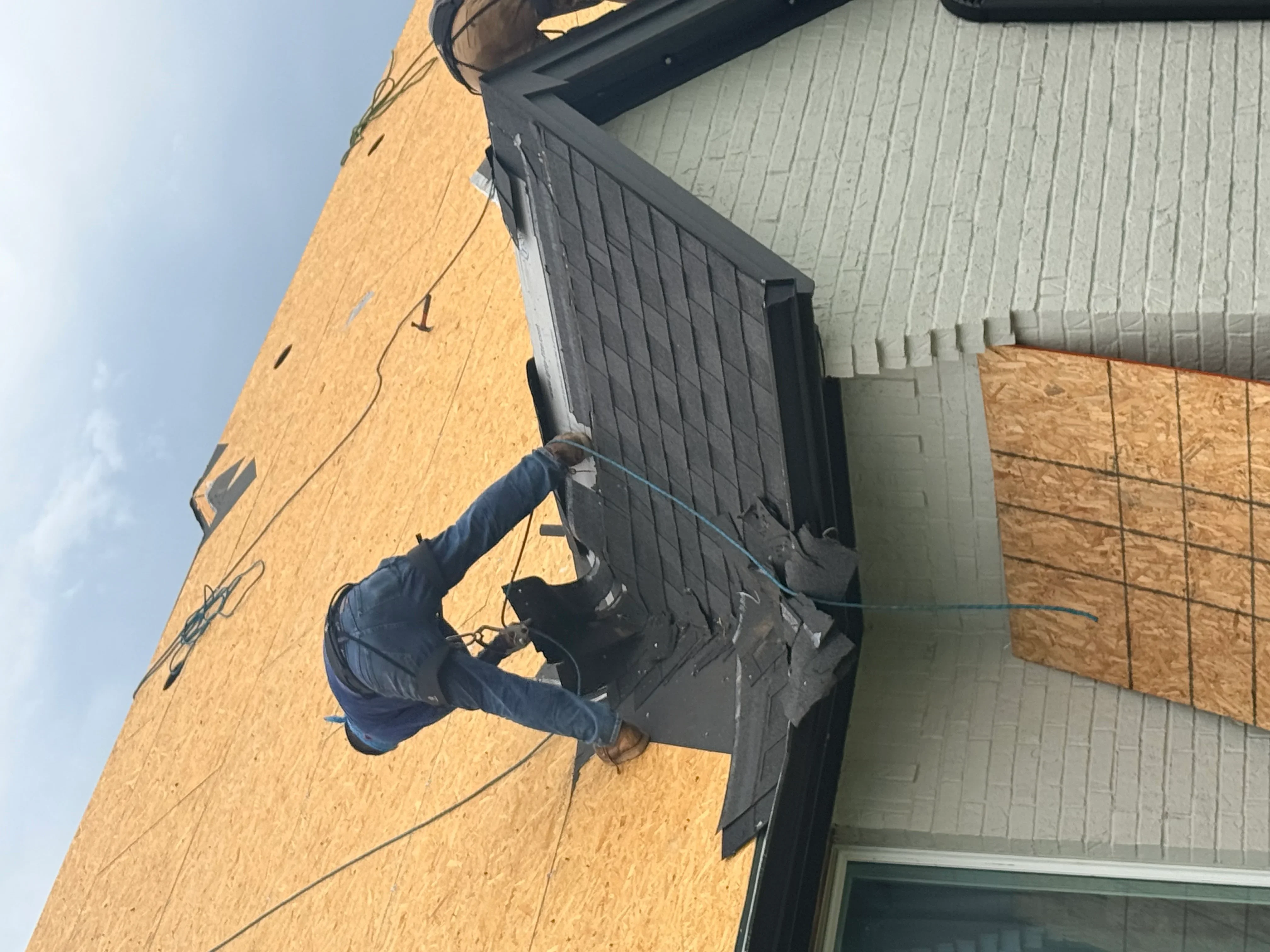 Roofer installing black architectural shingles on pitched roof with new soffit and fascia