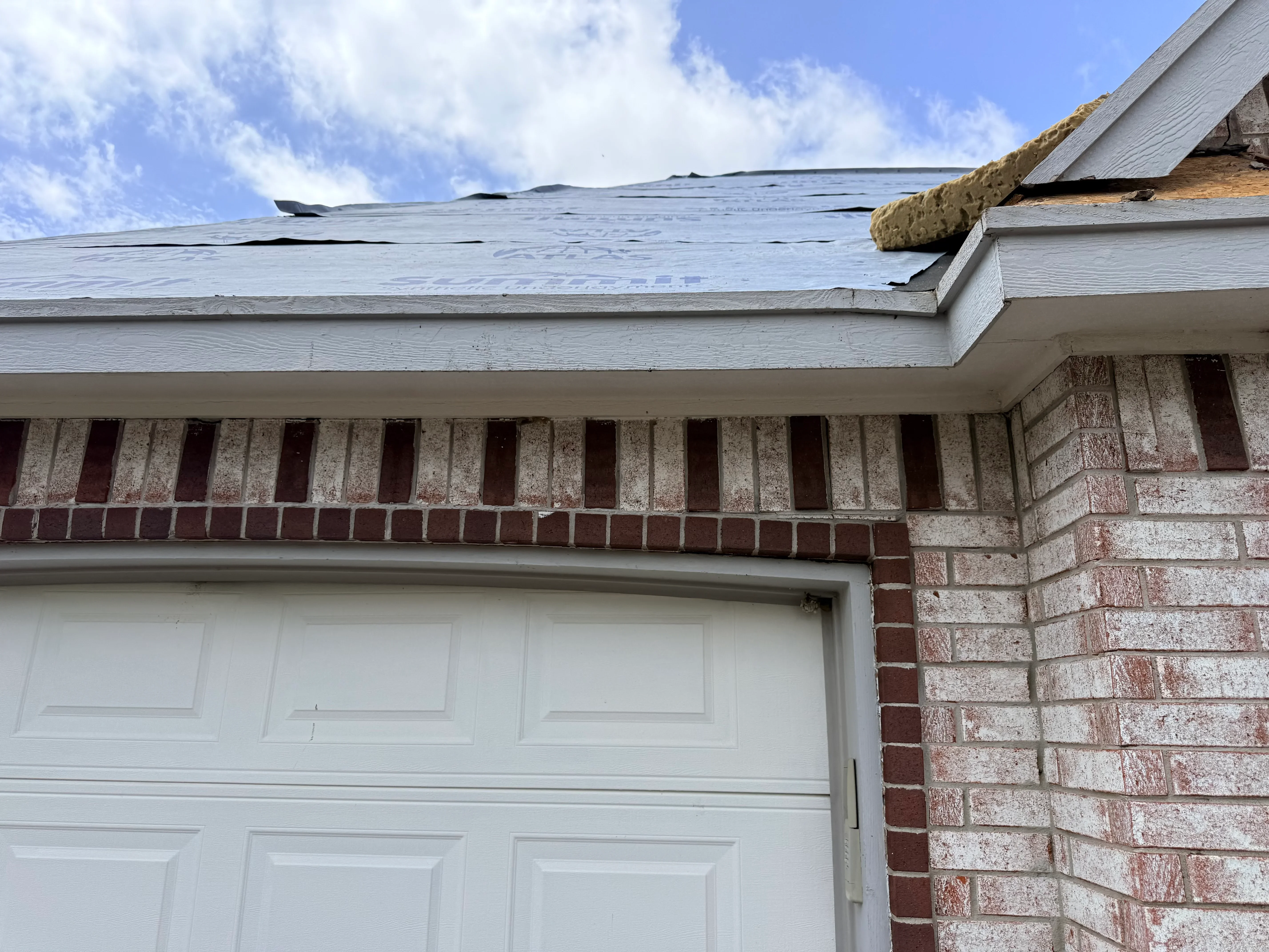 New asphalt shingle roof with insulation batts visible on brick home with white soffit and fascia