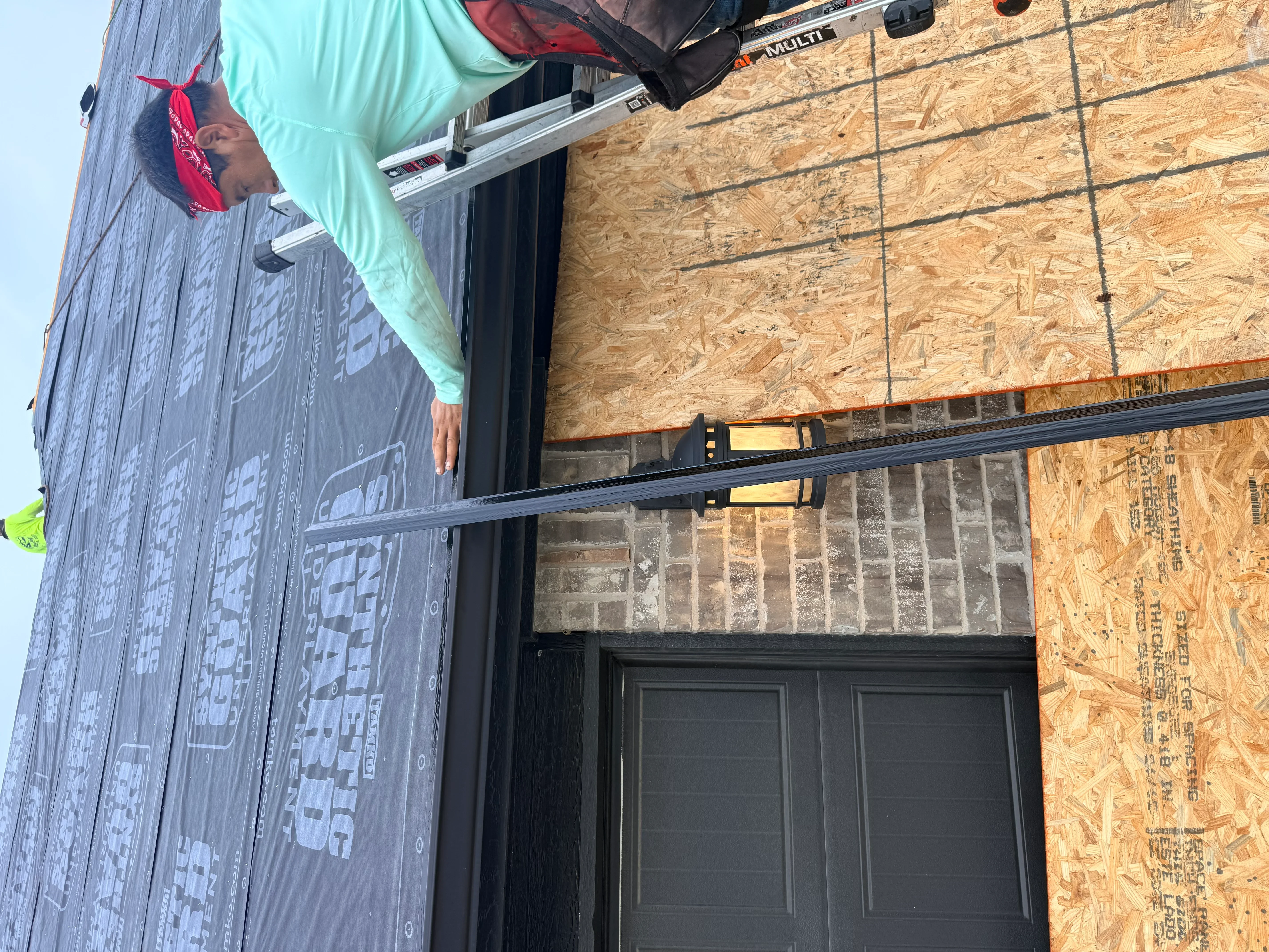Roofer installing OSB sheathing and underlayment with black drip edge trim on roof deck