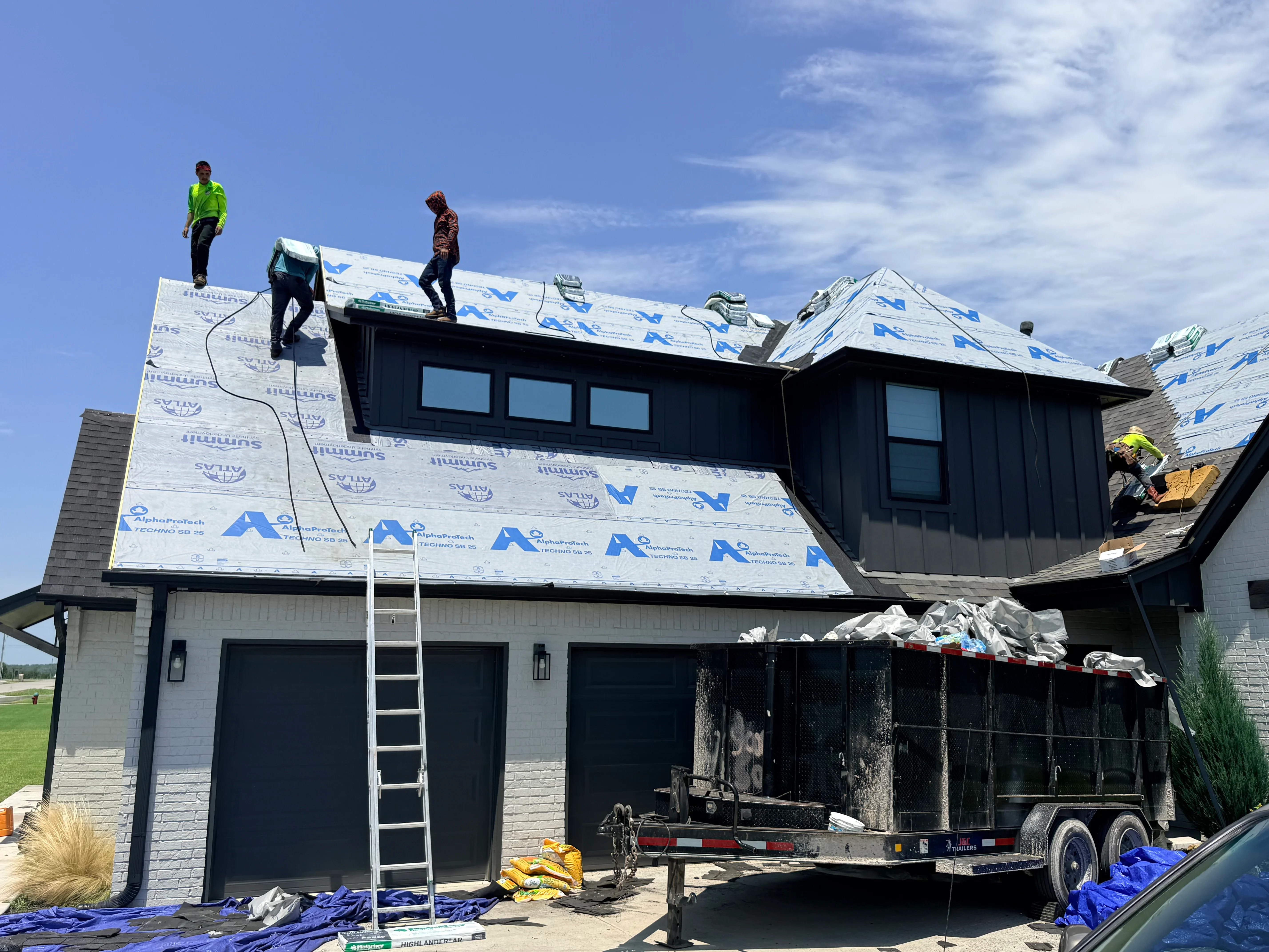 Roof installation with blue underlayment on modern home with dormers and skylights