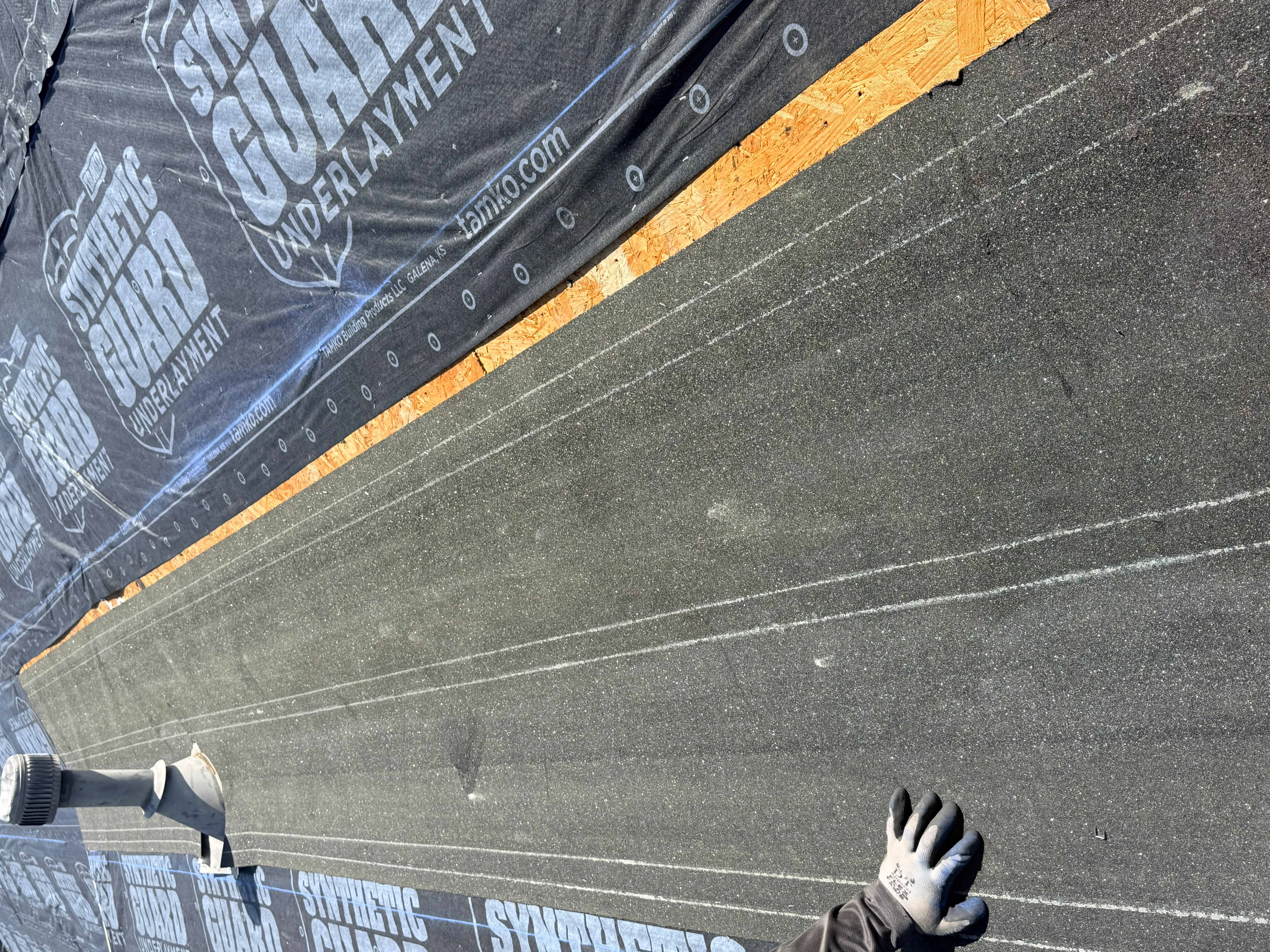 Asphalt shingles being installed over black underlayment with orange starter strip and chalk guide lines