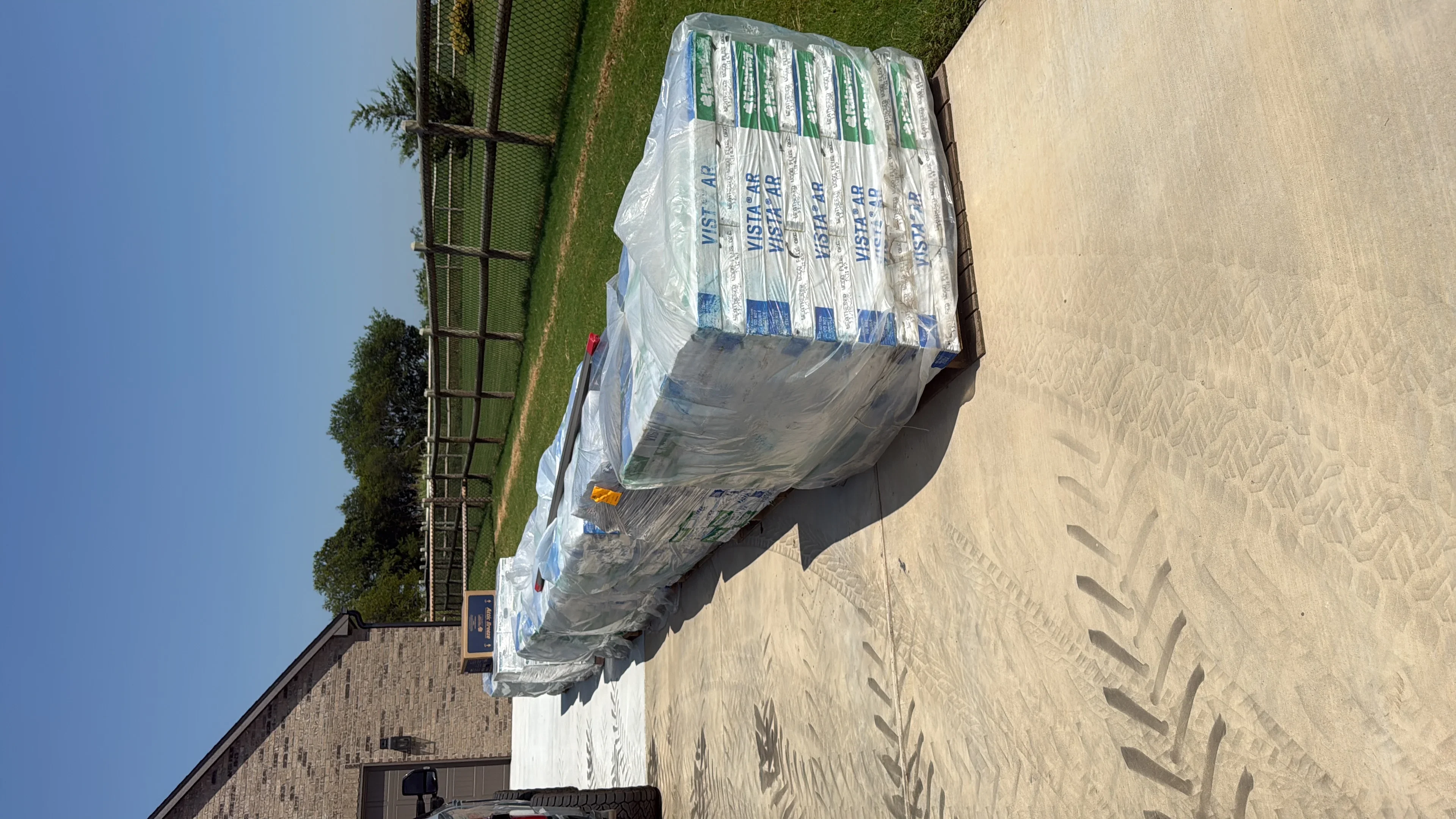 Stacked bundles of asphalt roofing shingles wrapped in plastic on residential driveway