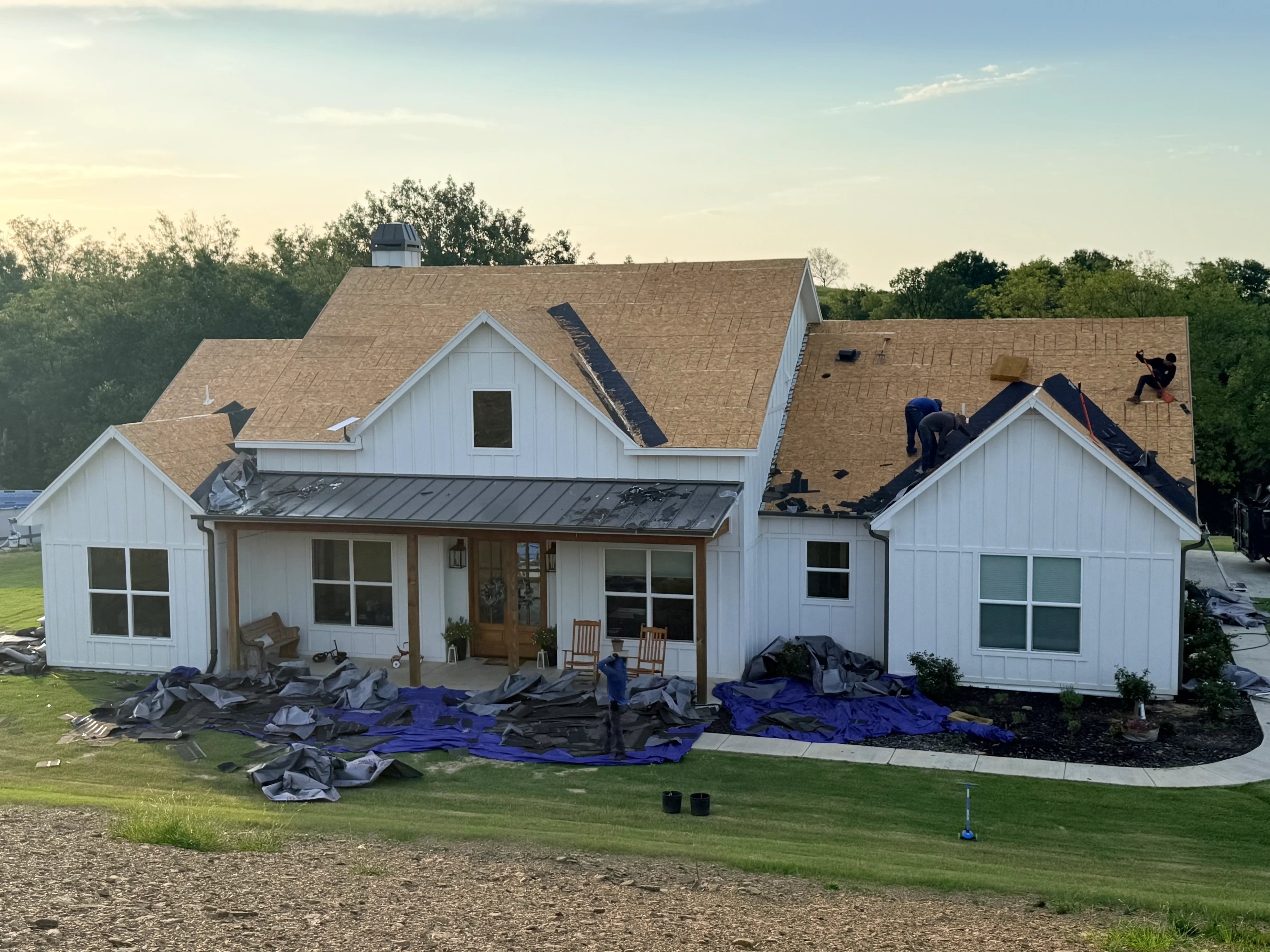 Architectural shingle roof installation on white farmhouse with multiple gables and metal accents