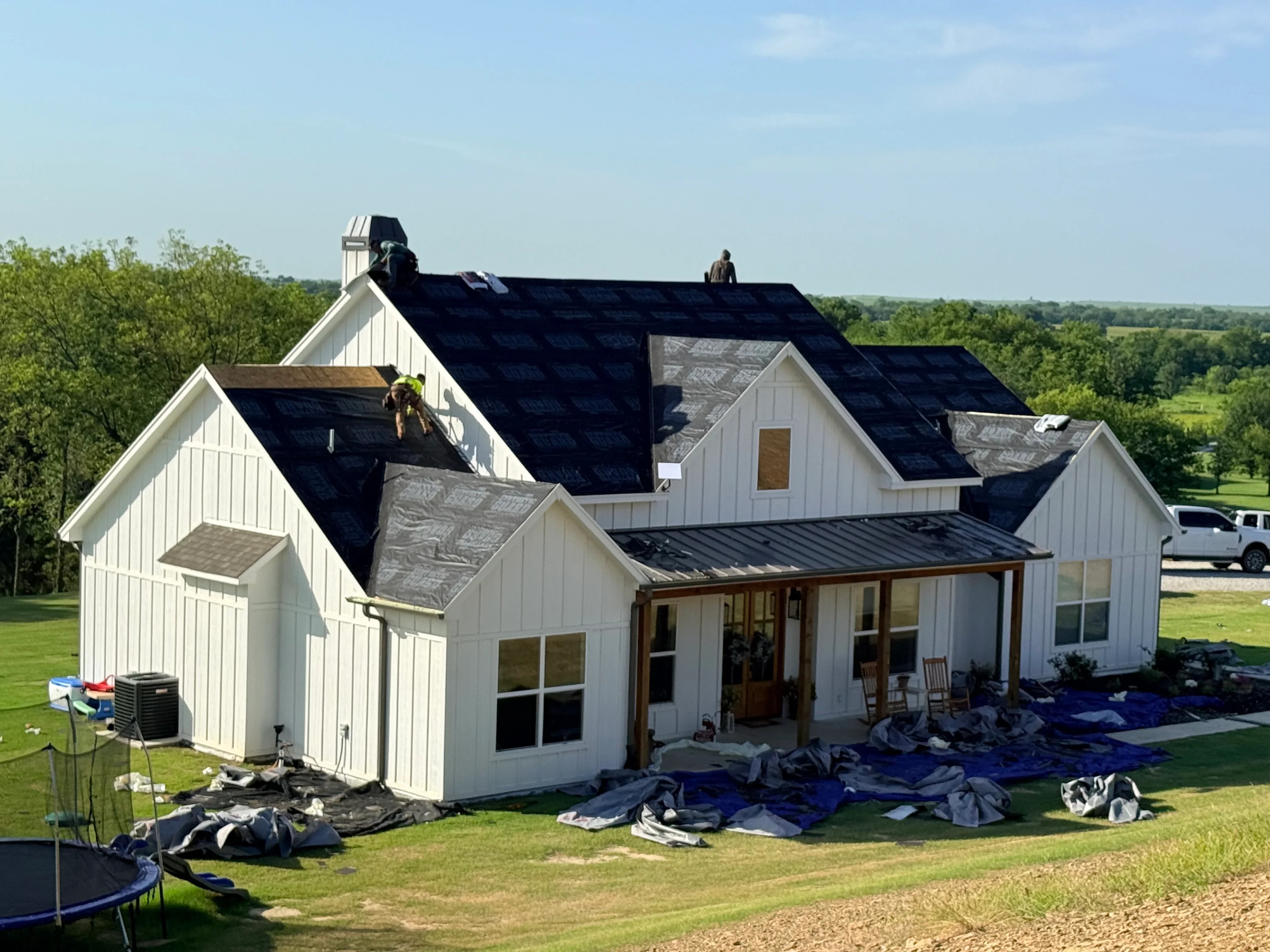 Dark asphalt shingle roof installation on white farmhouse with multiple dormers and roof planes
