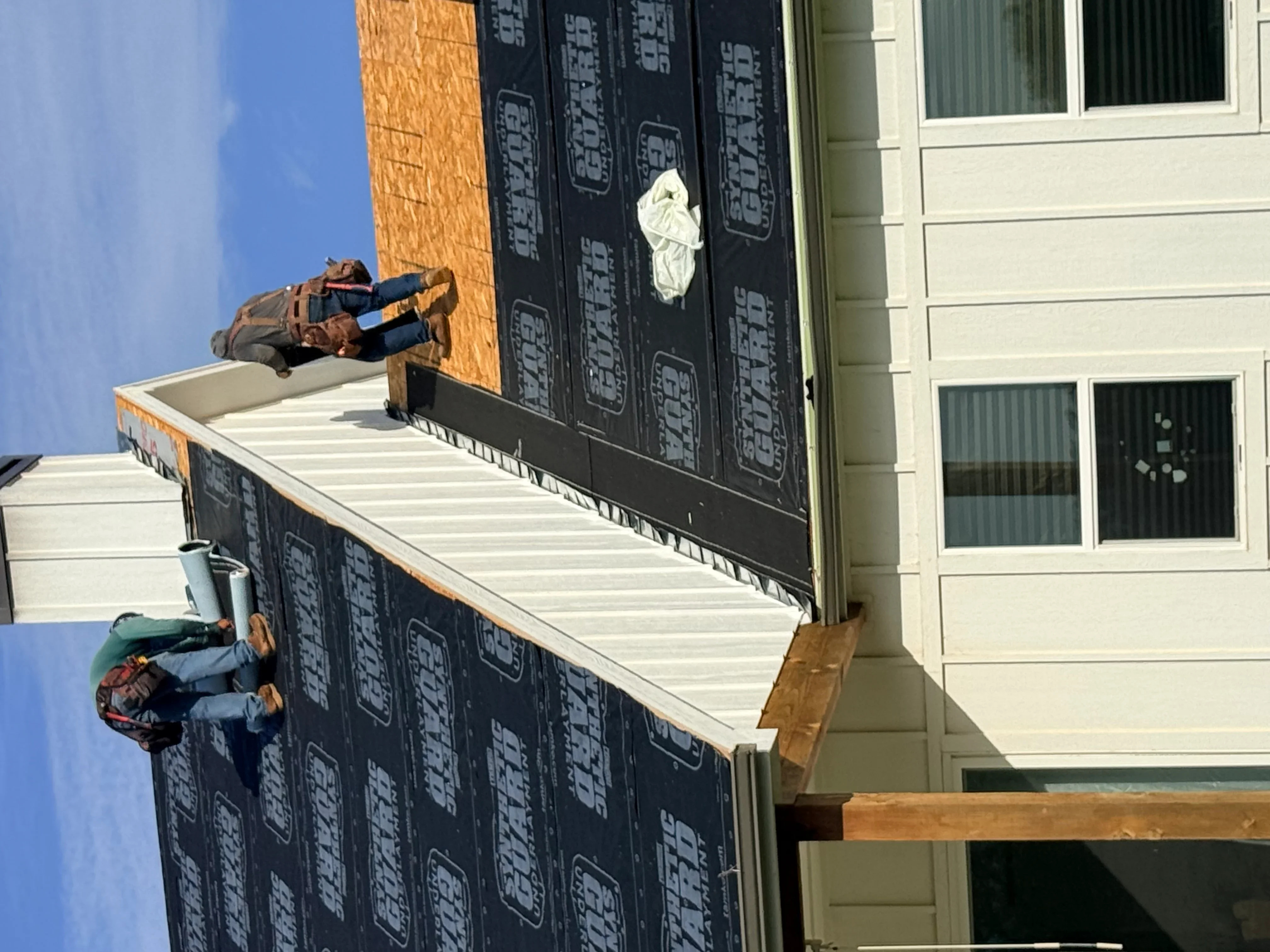 Roofers installing black shingles and underlayment on residential roof with metal flashing